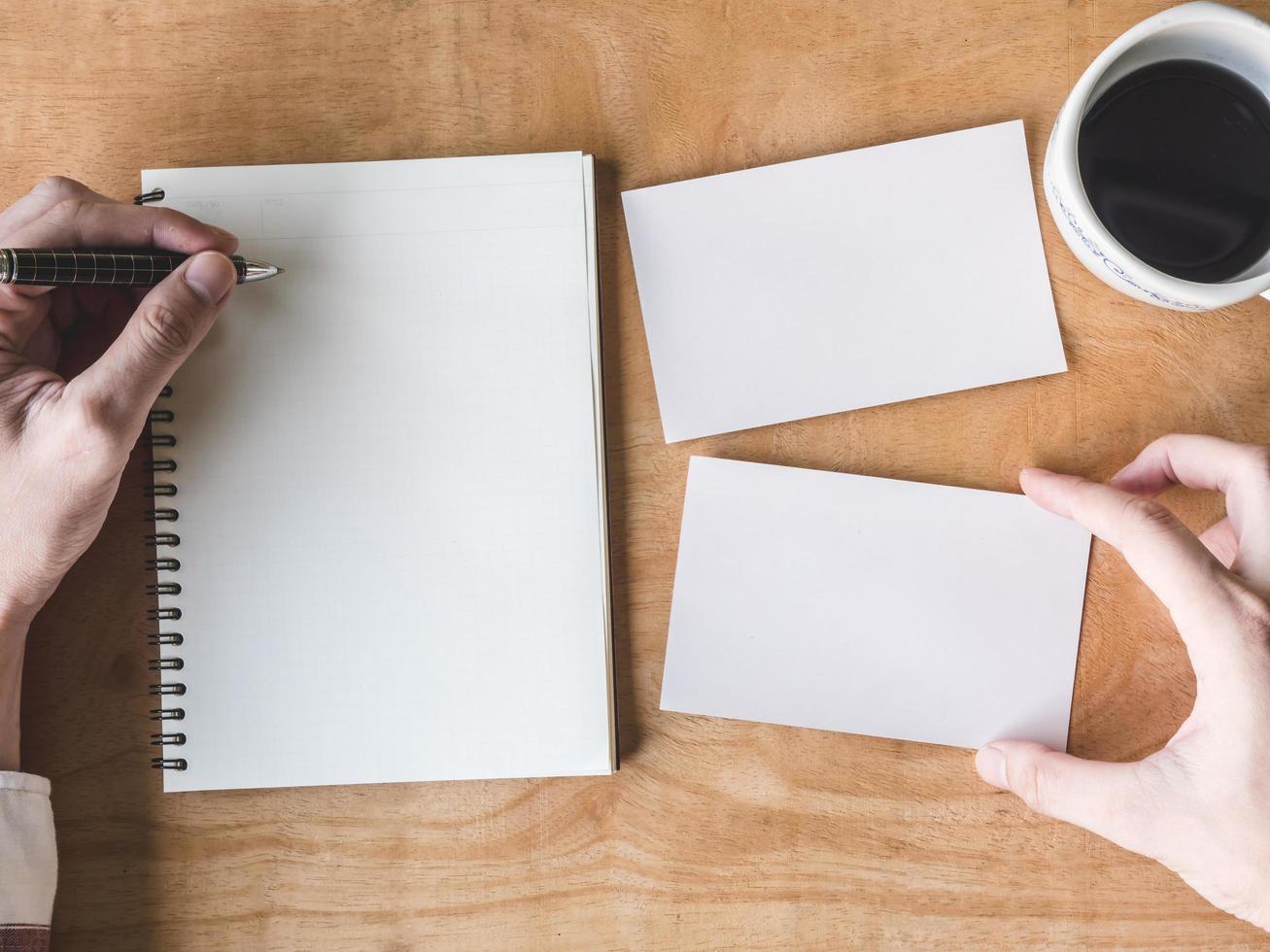top view of Male hands writing some data in notebook with blank photo cards and coffee cup on wooden table.
