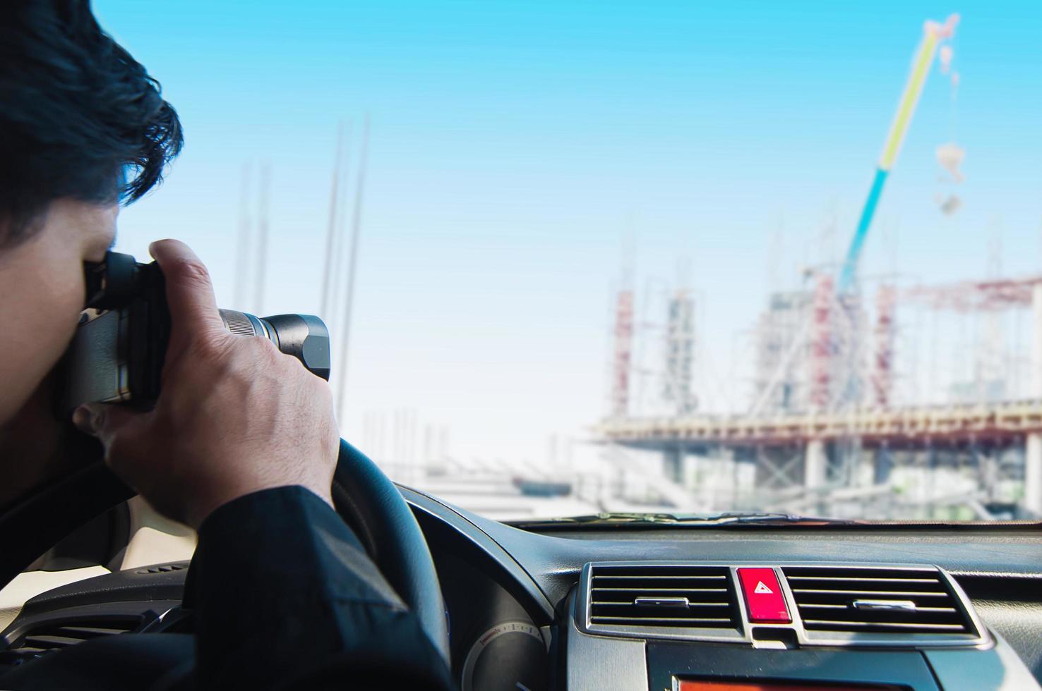 man take photo of construction site while driving in car - paparazzi or detective in car concept