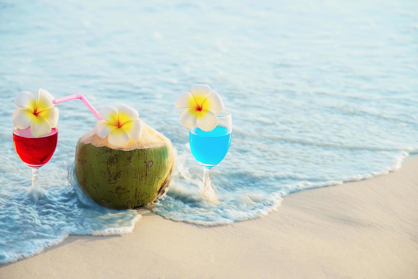 Cocktail glasses with coconut and pineapple on clean sand beach - fruit and drink on sea beach backgroudn concept photo