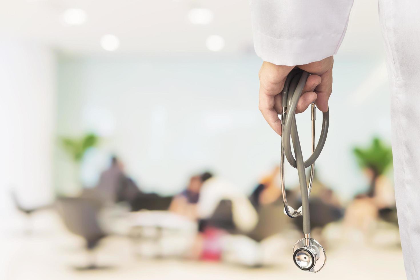 Doctor is going to examine his patient using his stethoscope over sitting people in modern hospital background photo