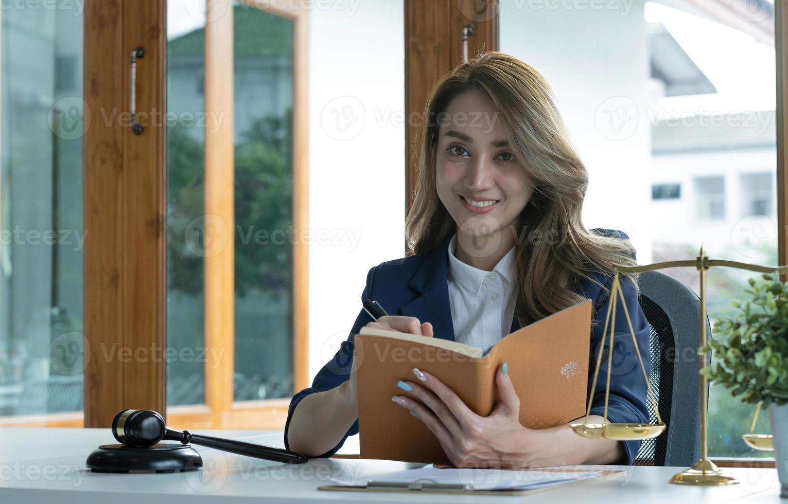 Confident and successful young Asian female lawyer or business legal consultant reading a law book or writing something on her notebook at her office desk. photo