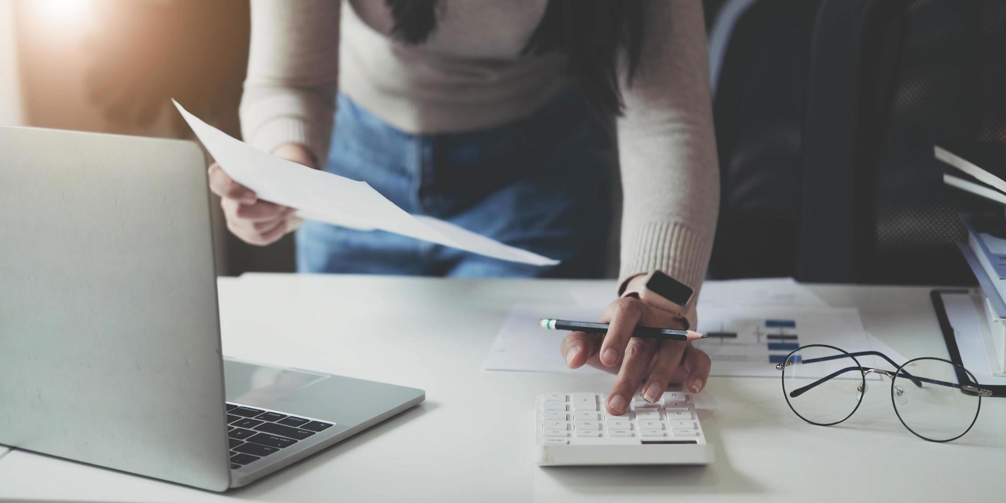 Finance Concept. Woman hold a graph pen, press a calculator and make money by writing reports, and memos, and analyzing business documents with a laptop computer vertically. photo