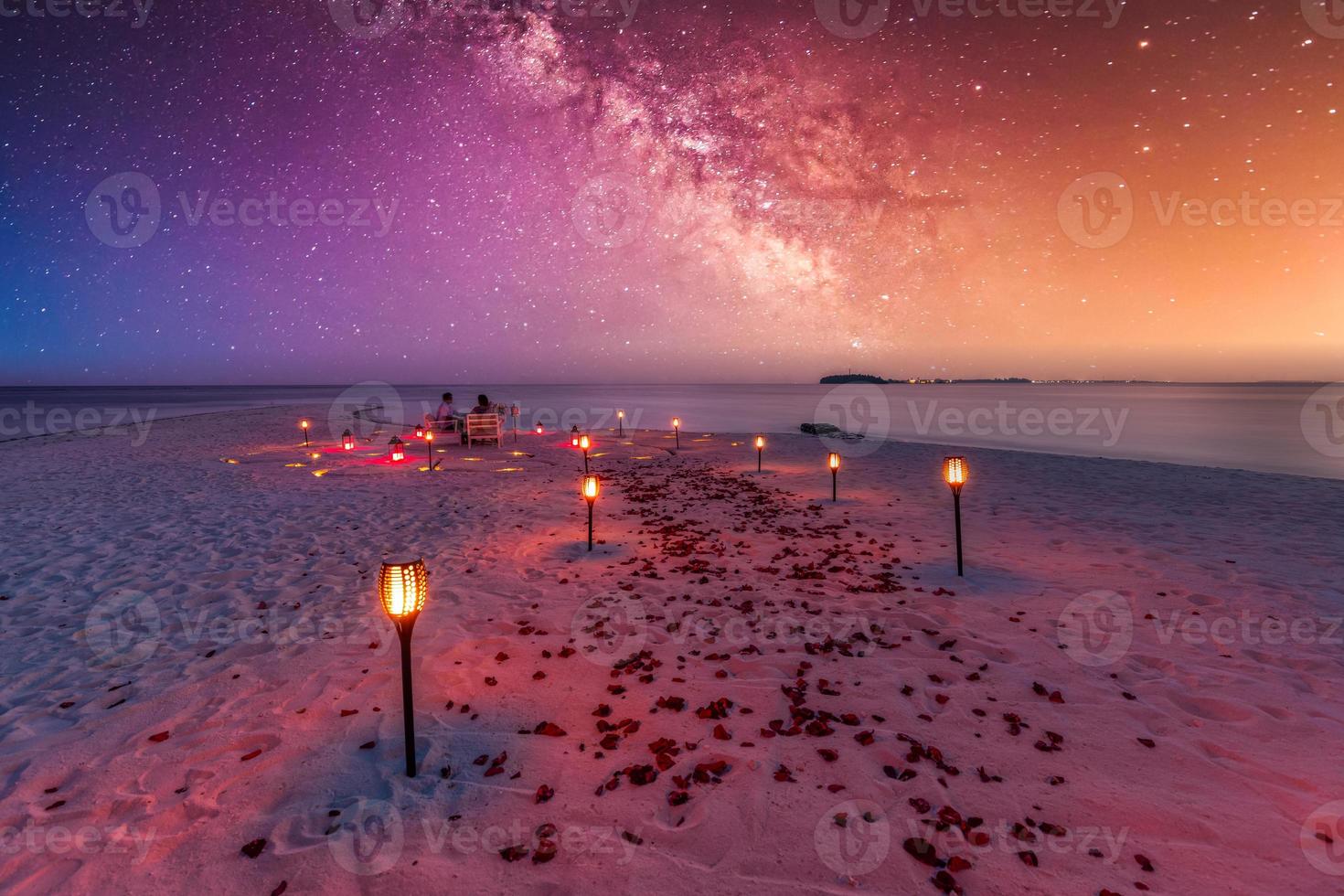 Destination dining, honeymoon, anniversary. Amazing romantic dinner beach on wooden deck with candles under sunset sky. Romance and love, luxury destination dinning, exotic table setup with sea view photo