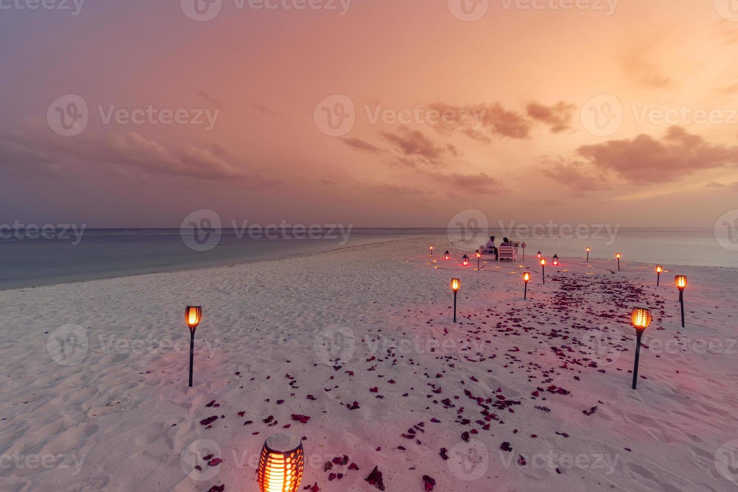 Destination dining, honeymoon, anniversary. Amazing romantic dinner beach on wooden deck with candles under sunset sky. Romance and love, luxury destination dinning, exotic table setup with sea view photo