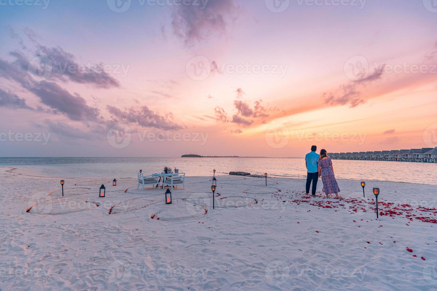 Destination dining, honeymoon, anniversary. Amazing romantic dinner beach on wooden deck with candles under sunset sky. Romance and love, luxury destination dinning, exotic table setup with sea view photo