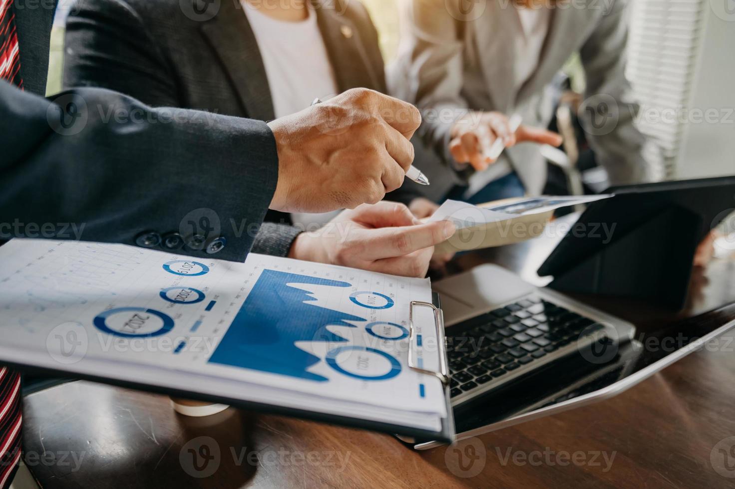 Business documents on office table with smart phone and laptop and two colleagues discussing data in the background photo