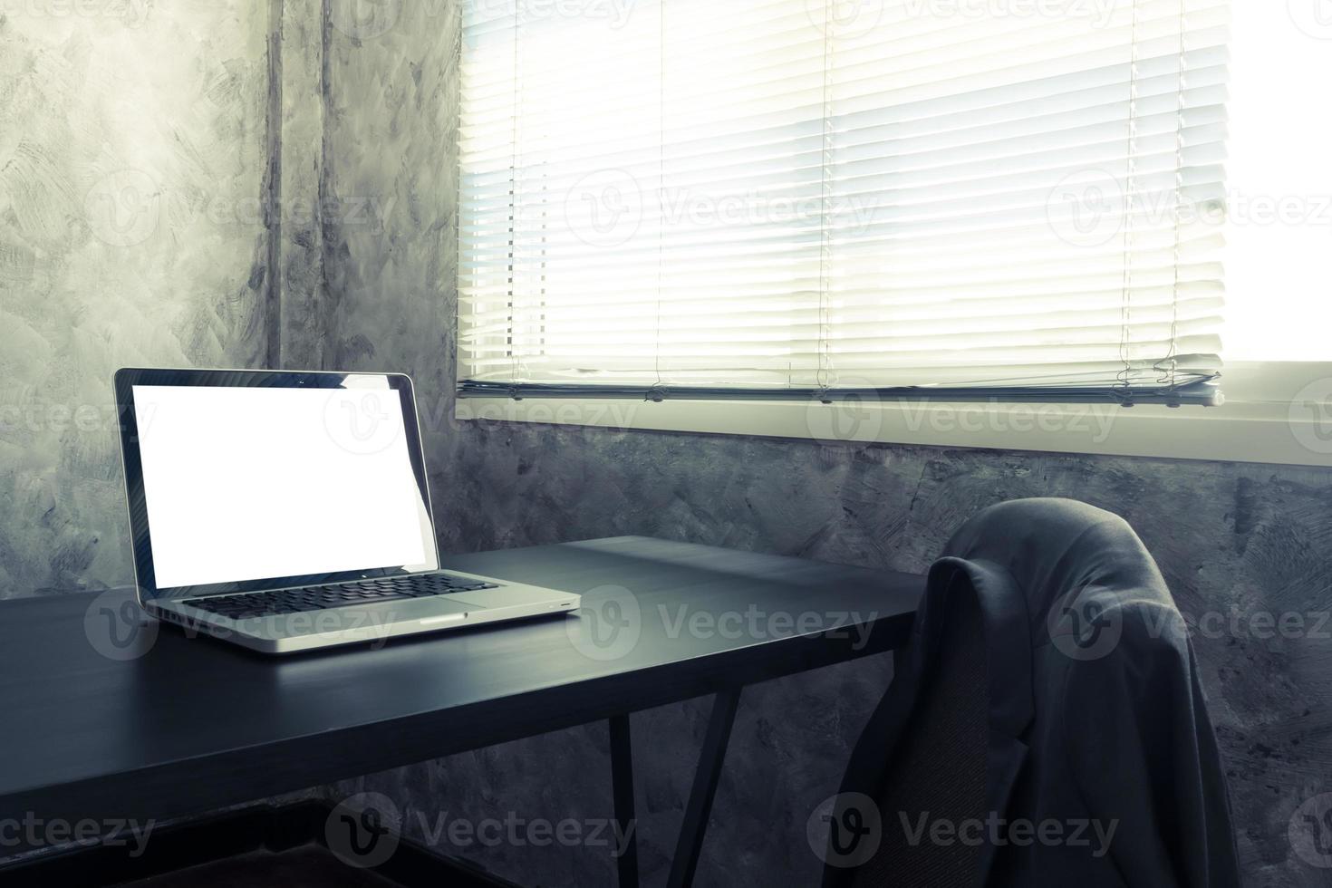 Laptop with white blank screen on the desk in the office room. Vintage tone photo