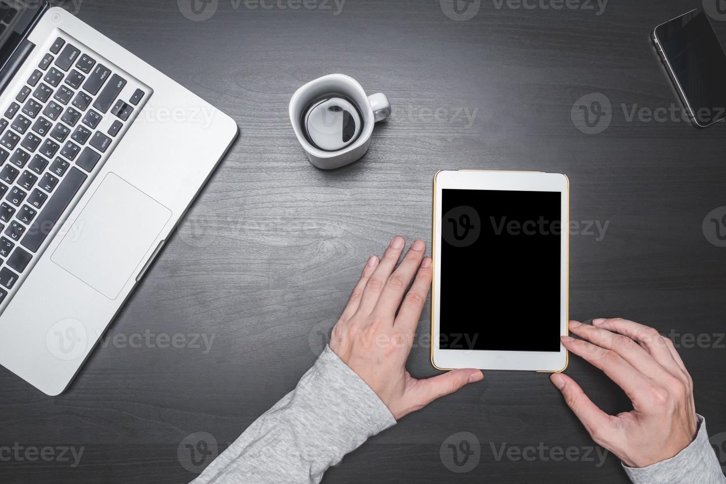 Top view of Male hands using Tablet with laptop,smart phone and coffee cup on black wooden table background. photo