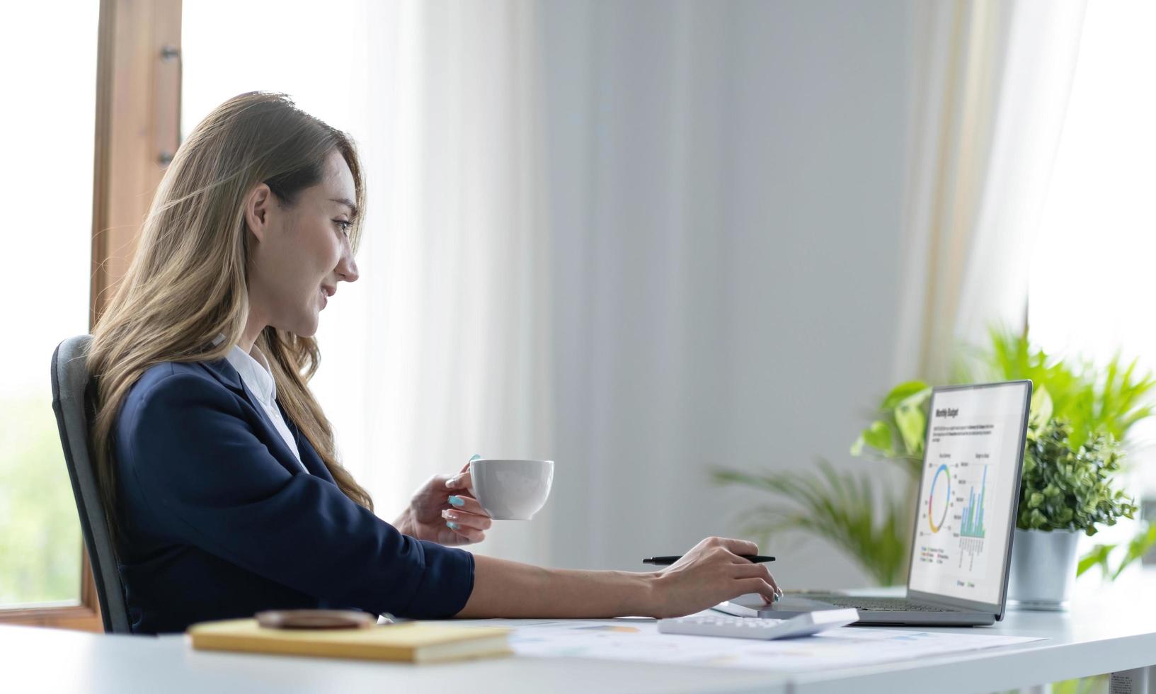 Beautiful young Asian businesswoman smiling holding a coffee mug and laptop working at the office. photo