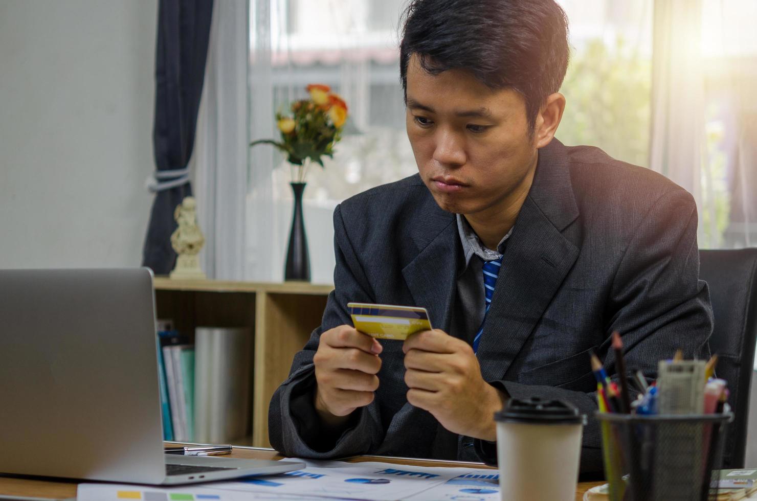 Businessman holding a credit card looking at documents graphs finances and economic investments at the computer with anxiety planning and online shopping with stress. photo