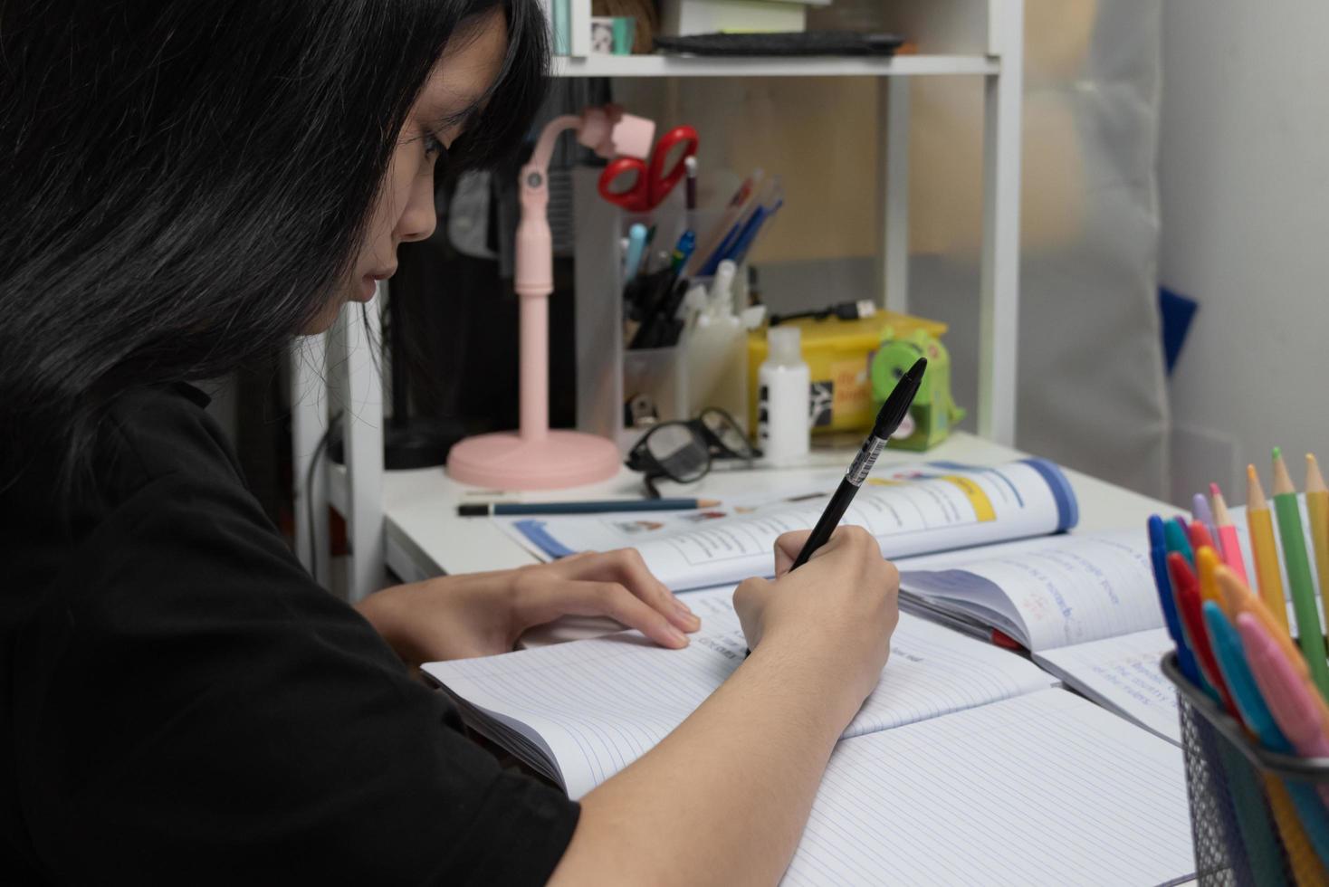 Asian student girl is writing homework and reading book at desk photo