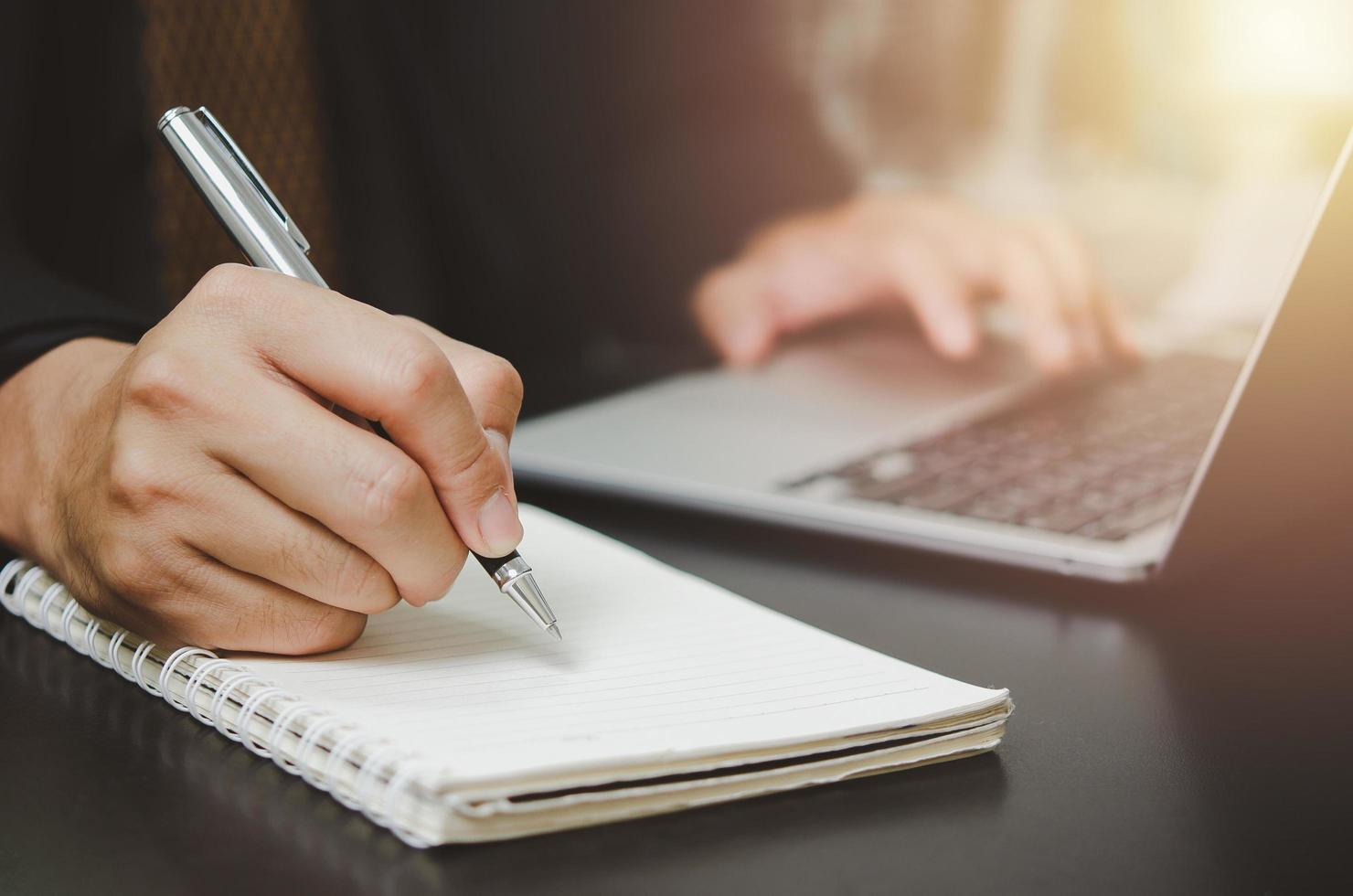 persona hombre sosteniendo un bolígrafo escribir un plan o una idea en un libro con una computadora portátil en el escritorio. foto