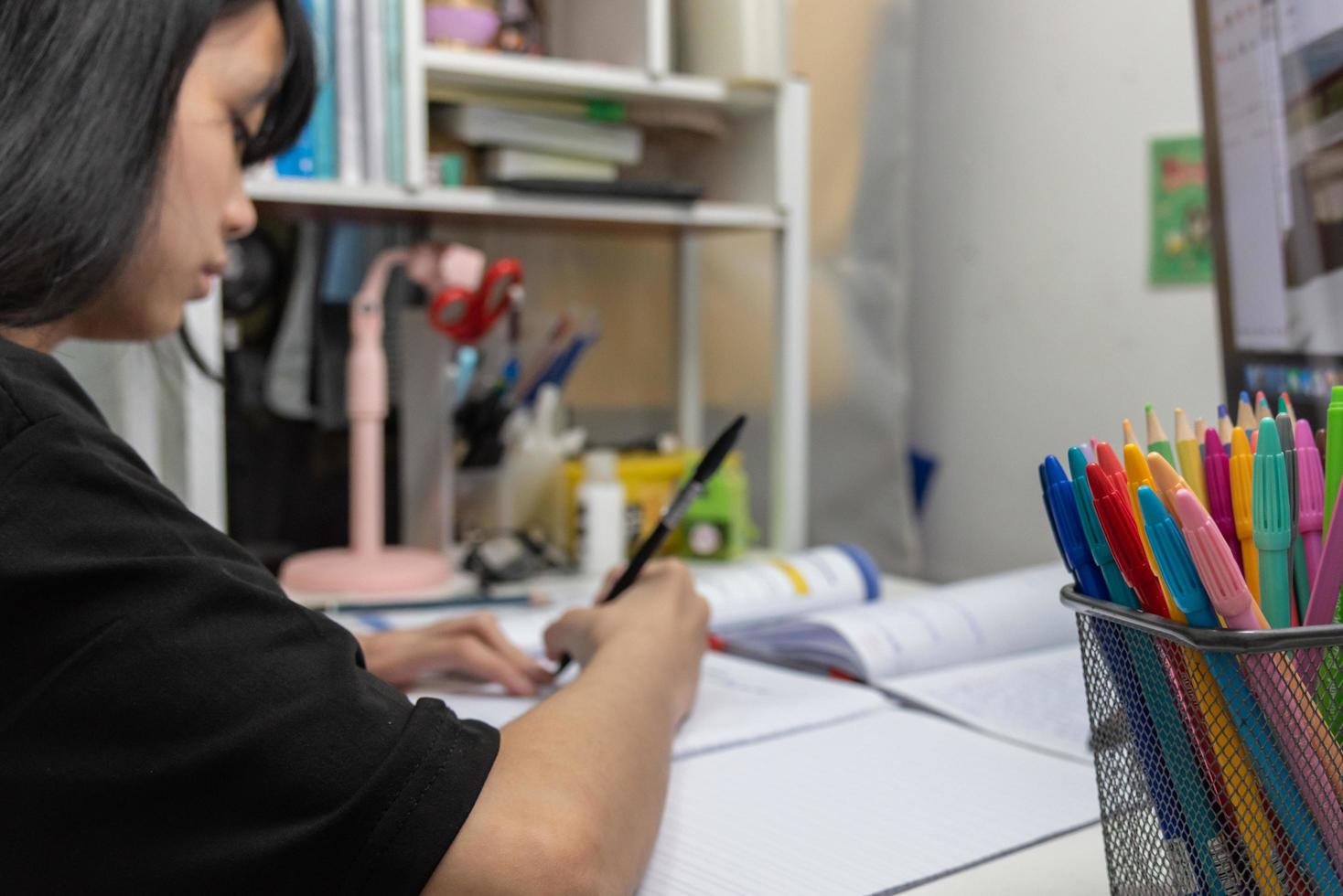 una estudiante asiática está escribiendo deberes y leyendo un libro en el escritorio foto