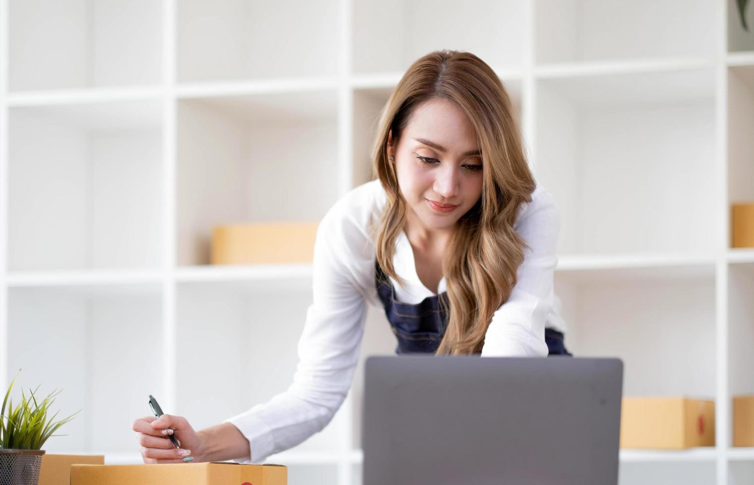 startup sme pequeña empresaria sme o mujer asiática independiente que usa una computadora portátil con caja, joven mujer asiática de éxito con su mano levantada, caja de embalaje de marketing en línea y entrega, concepto sme. foto