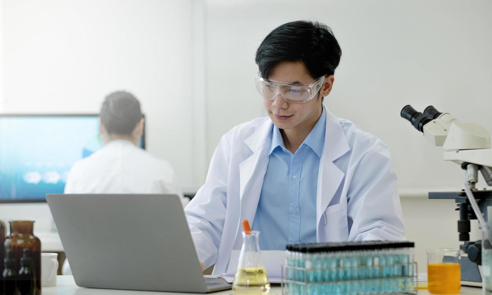 retrato de laboratorio de investigación médica de un apuesto científico masculino que usa una tableta digital, analizando bioquímicos líquidos en un matraz de laboratorio. foto