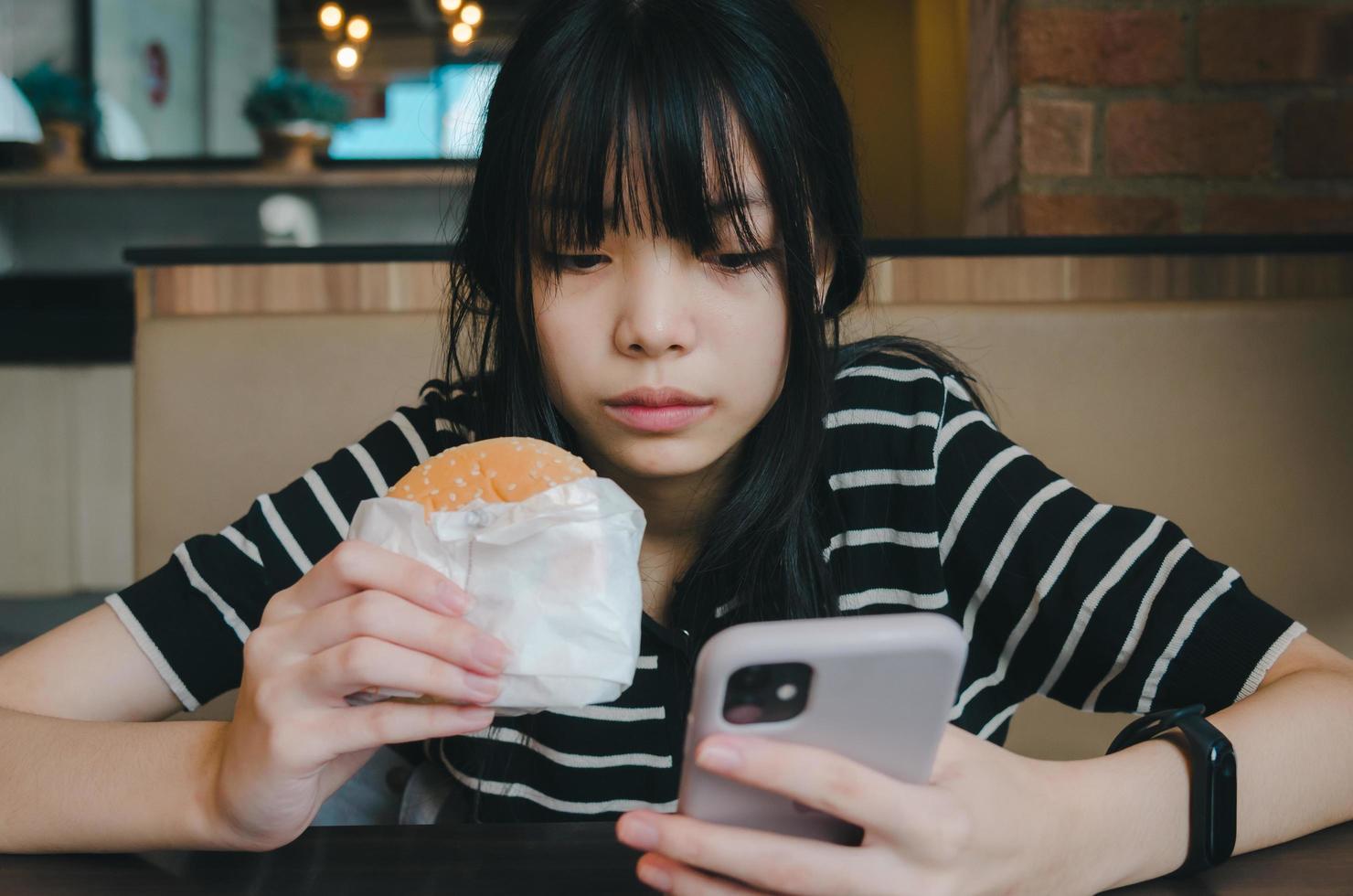 Female person holding mobile smartphone social network internet technology and eat hamburger fast food. photo