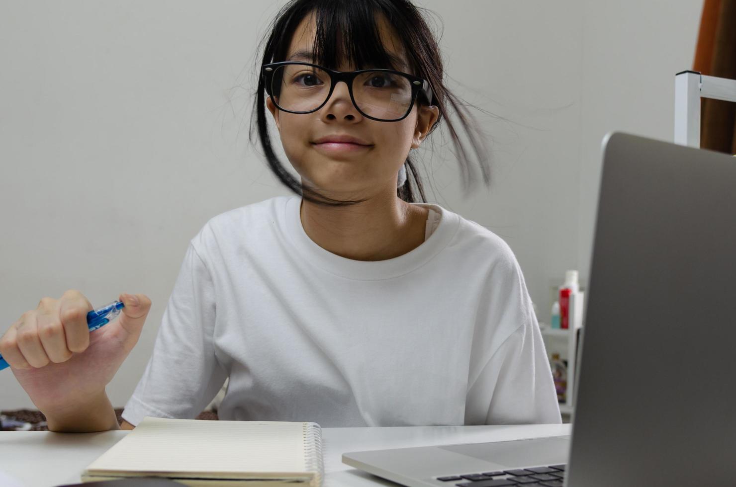 girl holding pen writing book study learning digital internet video online computer laptop at home. photo