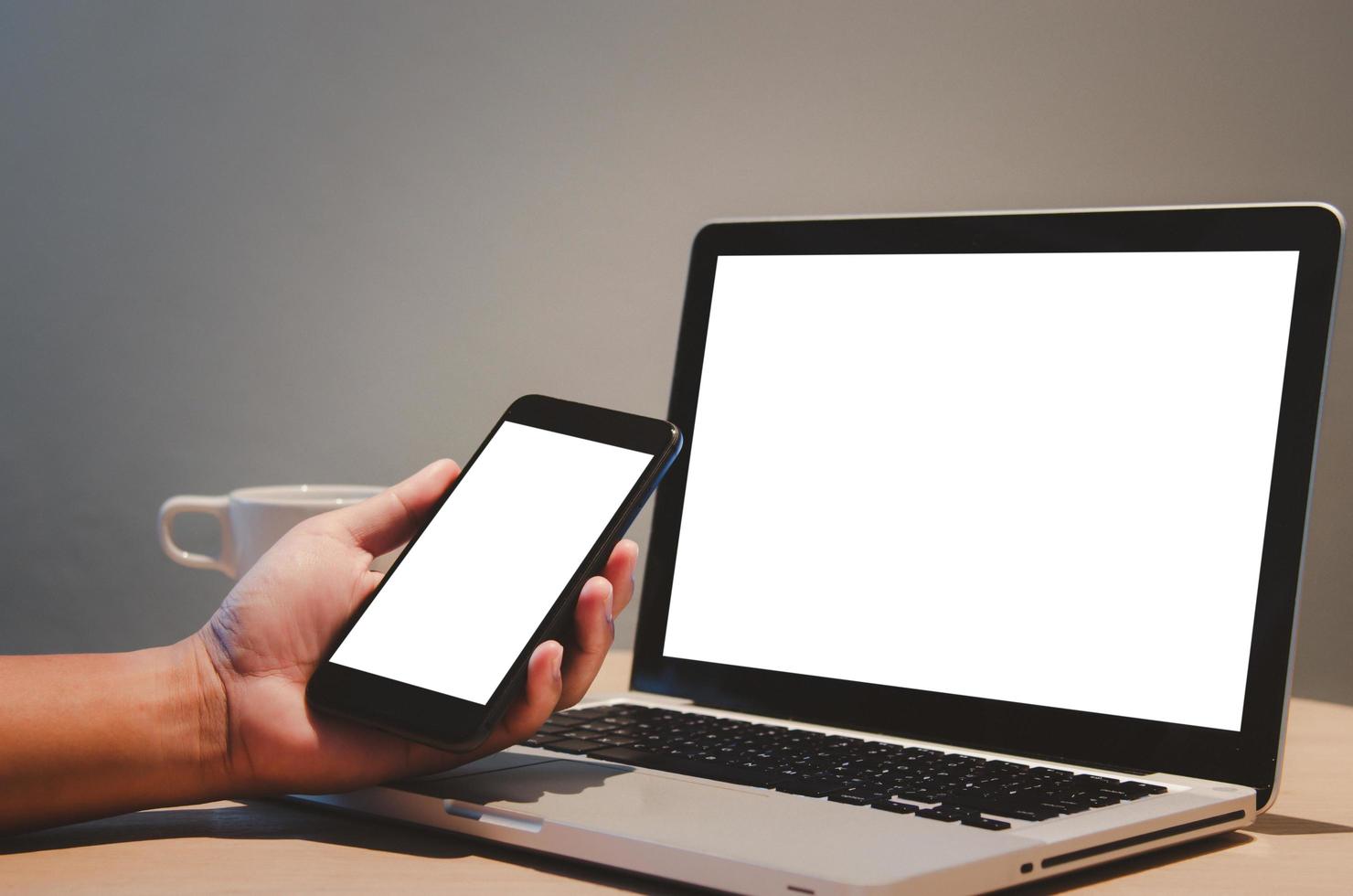 man hand holding mobile smartphone and computer laptop mock up blank screen on desk. photo