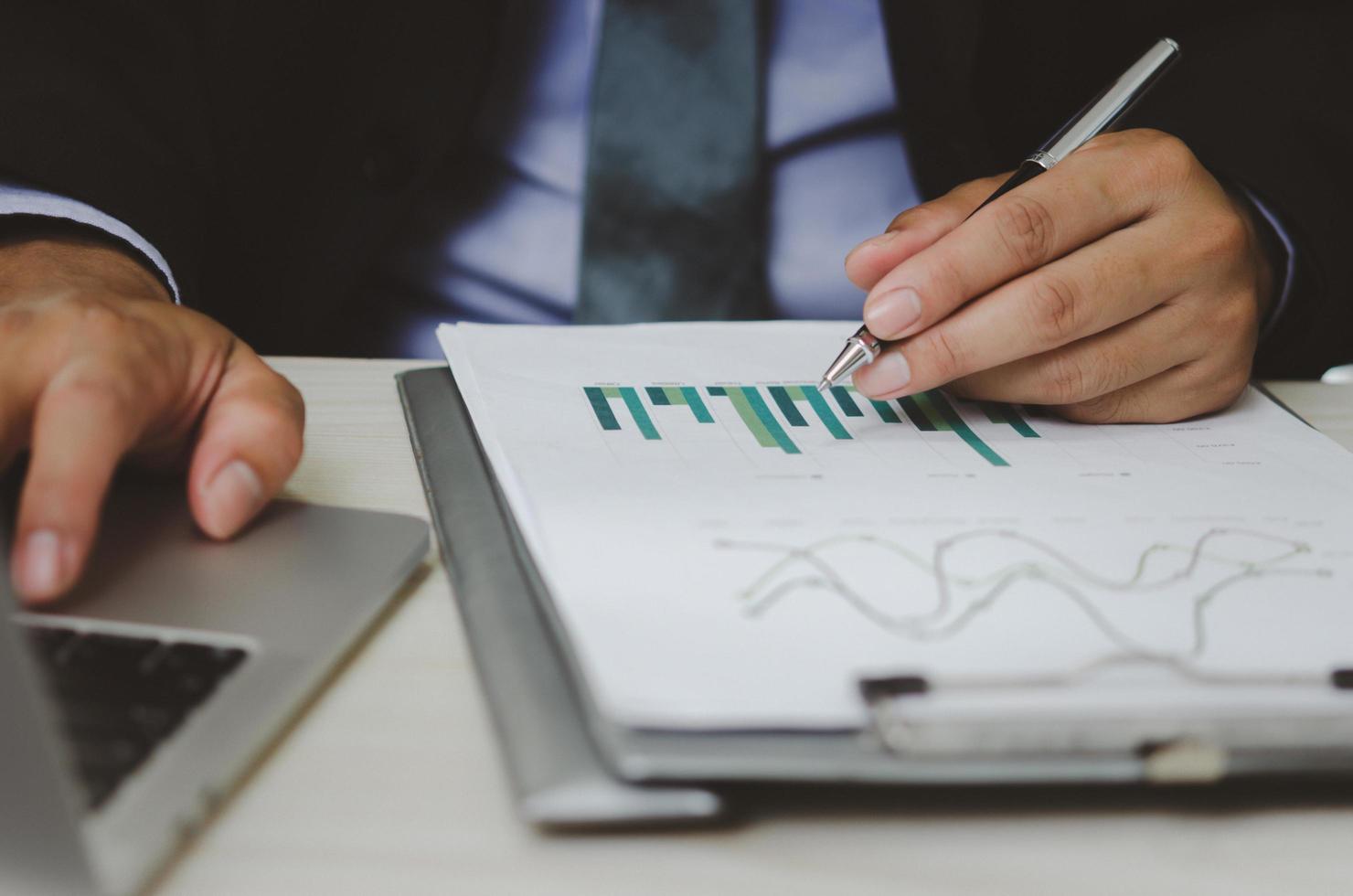 hombre de negocios que sostiene la pluma para trabajar gráficos y tablas de computadora datos datos estadísticos documentos de análisis financiero. foto