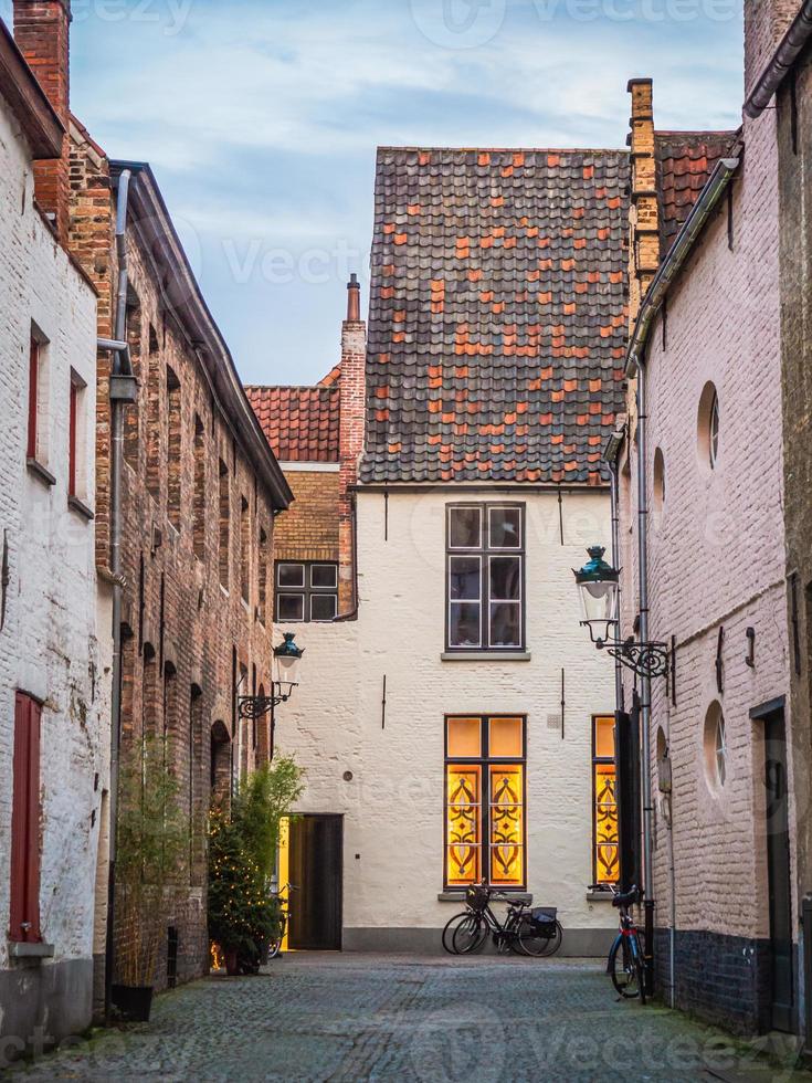 The front view of a beautiful house with its cute roof made of red and black bricks on a narrow street in Bruges, Belgium. photo