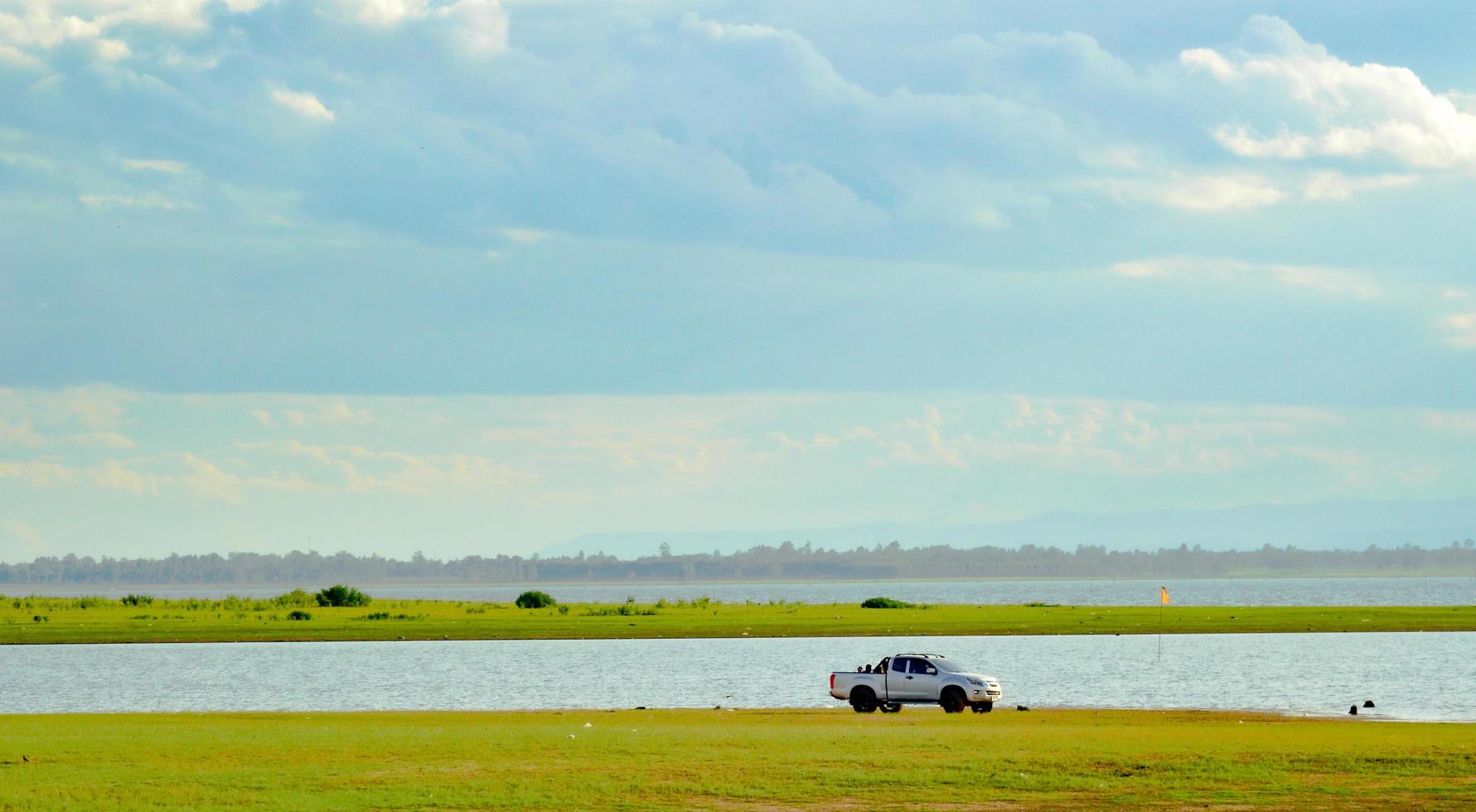 Lake landscape with a pickup truck on a green grassy mound.  distant mountains  The sky is full of black clouds. Holiday travel concept. photo