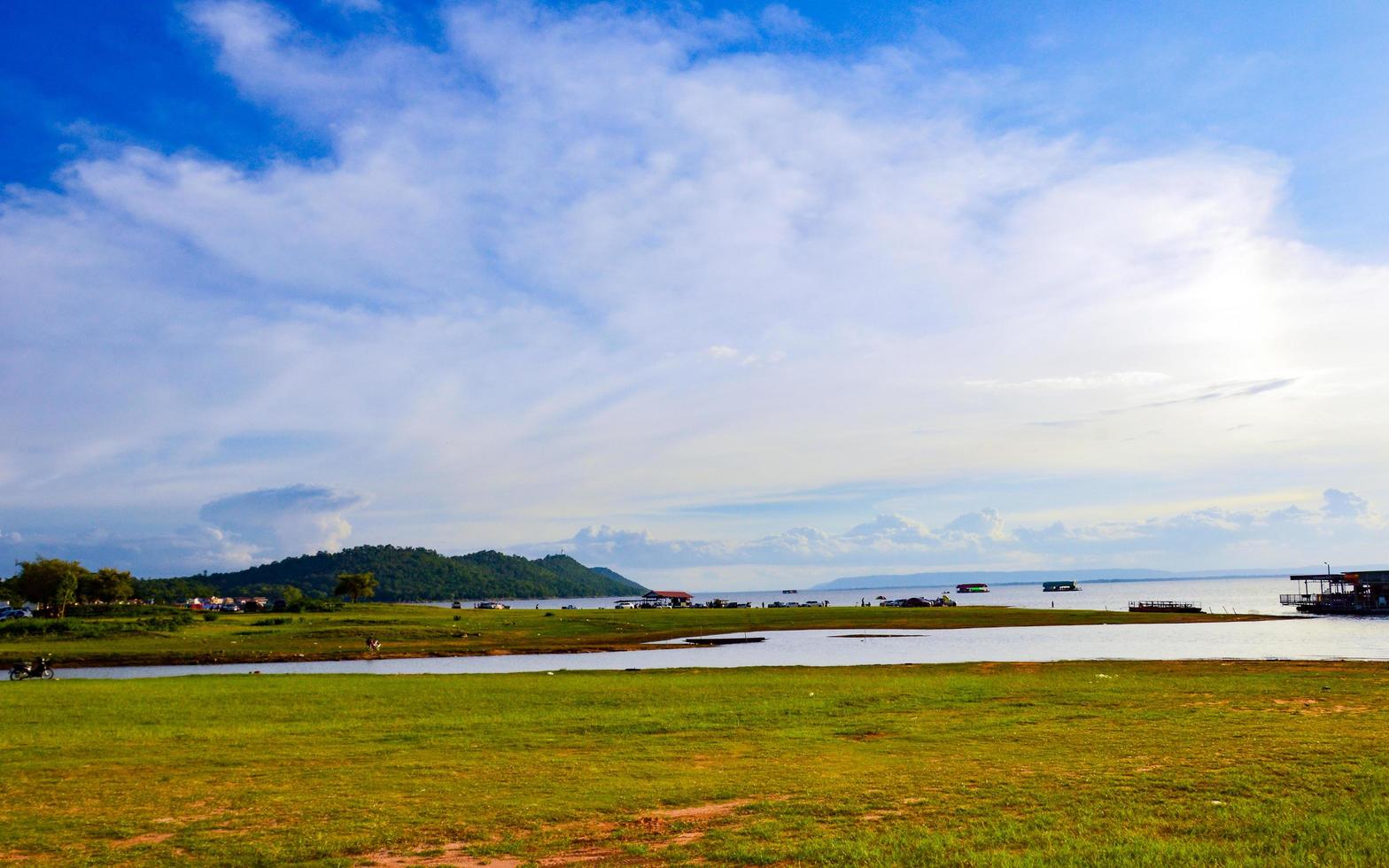 Lake landscape with mounds covered with green grass and trees.  There is a raft in the middle of the water  blue sky with white clouds on a sunny day holiday photo