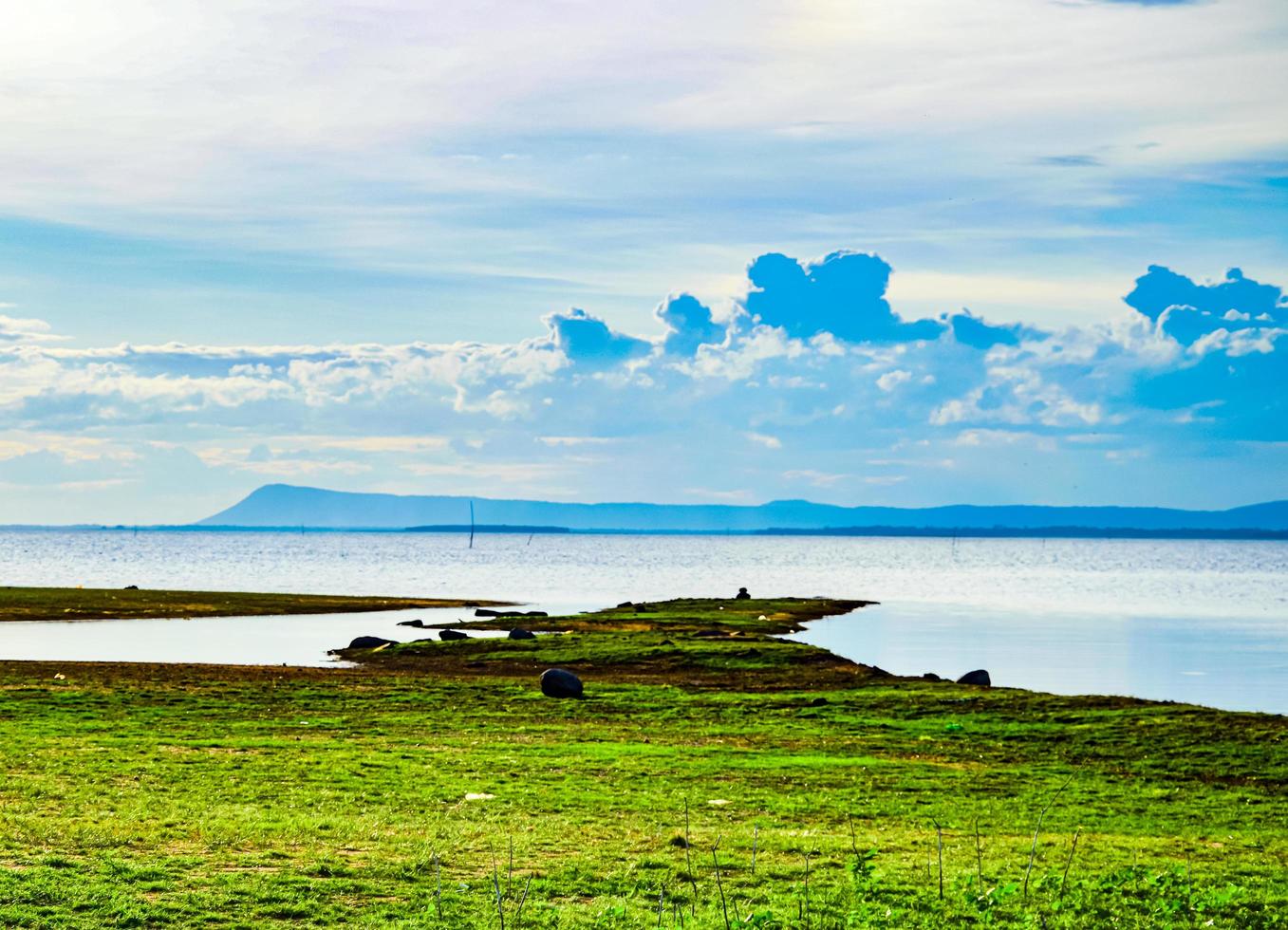 lake scenery  There is a mound covered with green grass.  A distant mountain near the horizon where black rain clouds were forming in the  day with inclement weather photo