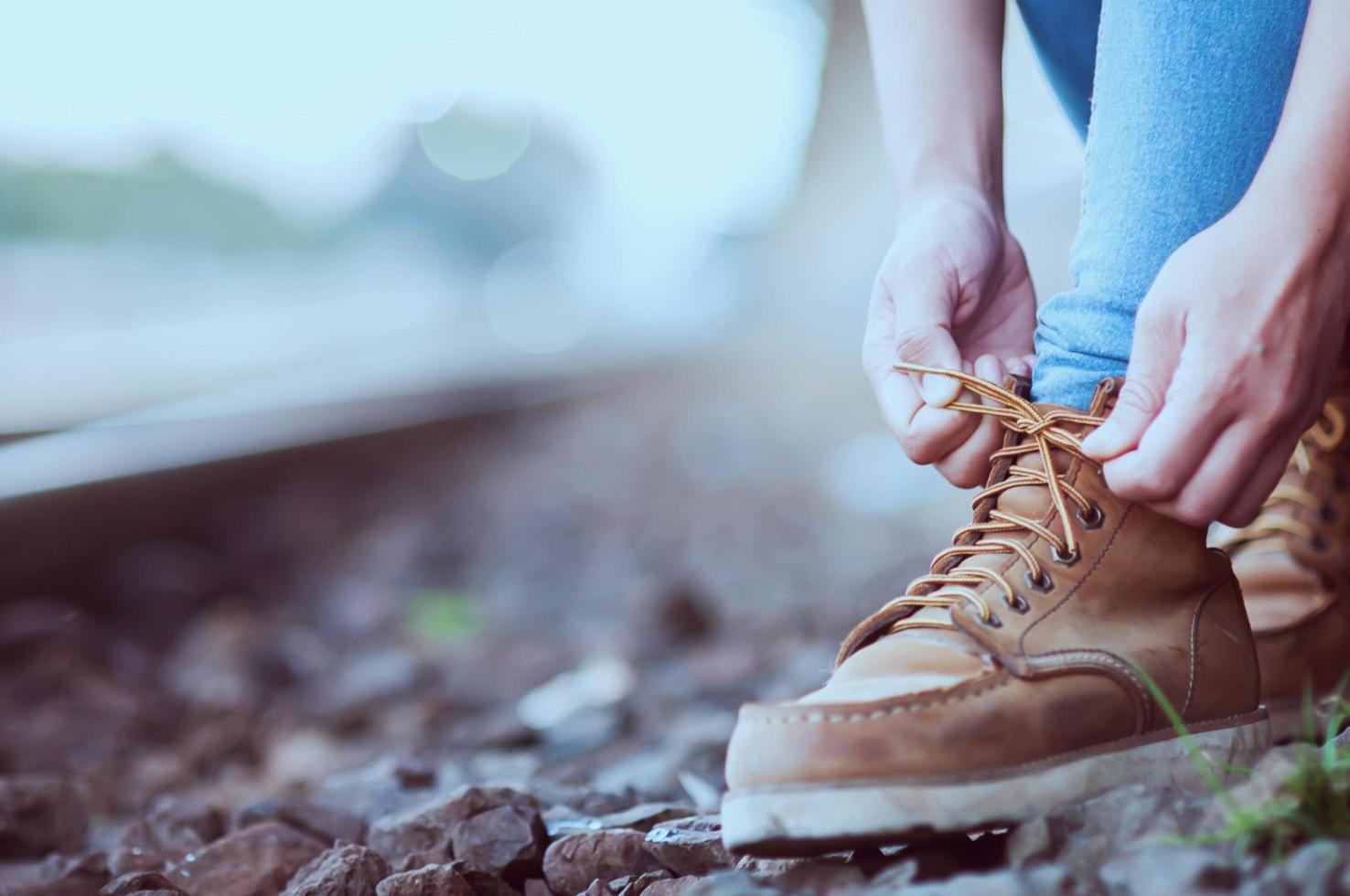 Unknown lady tying his shoelaces on a stone way near the train rail photo