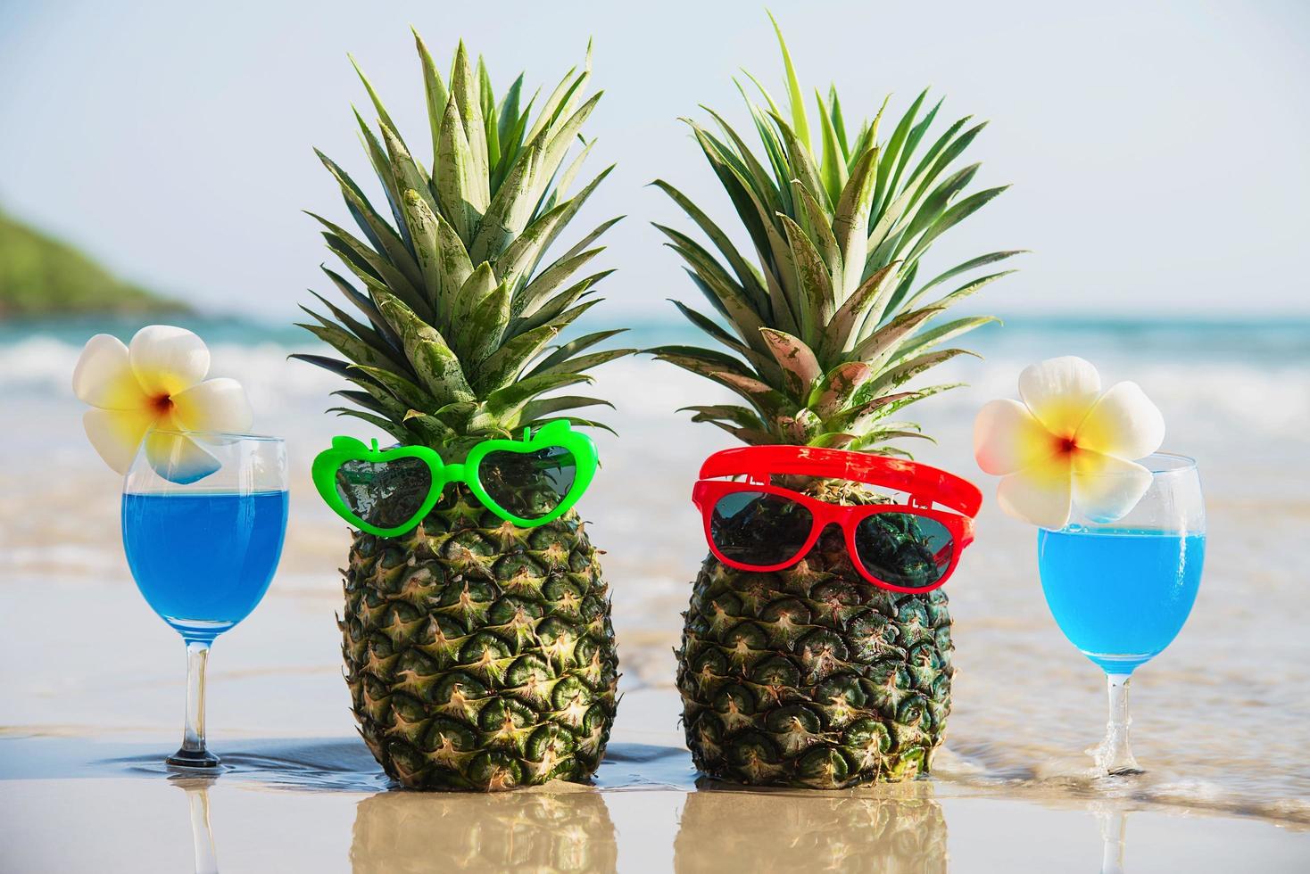 Fresh couple pineapples with sun glasses and cocktail glasses on clean sand beach with sea wave background - fresh fruit and drink with sea sand sun vacation background concept photo