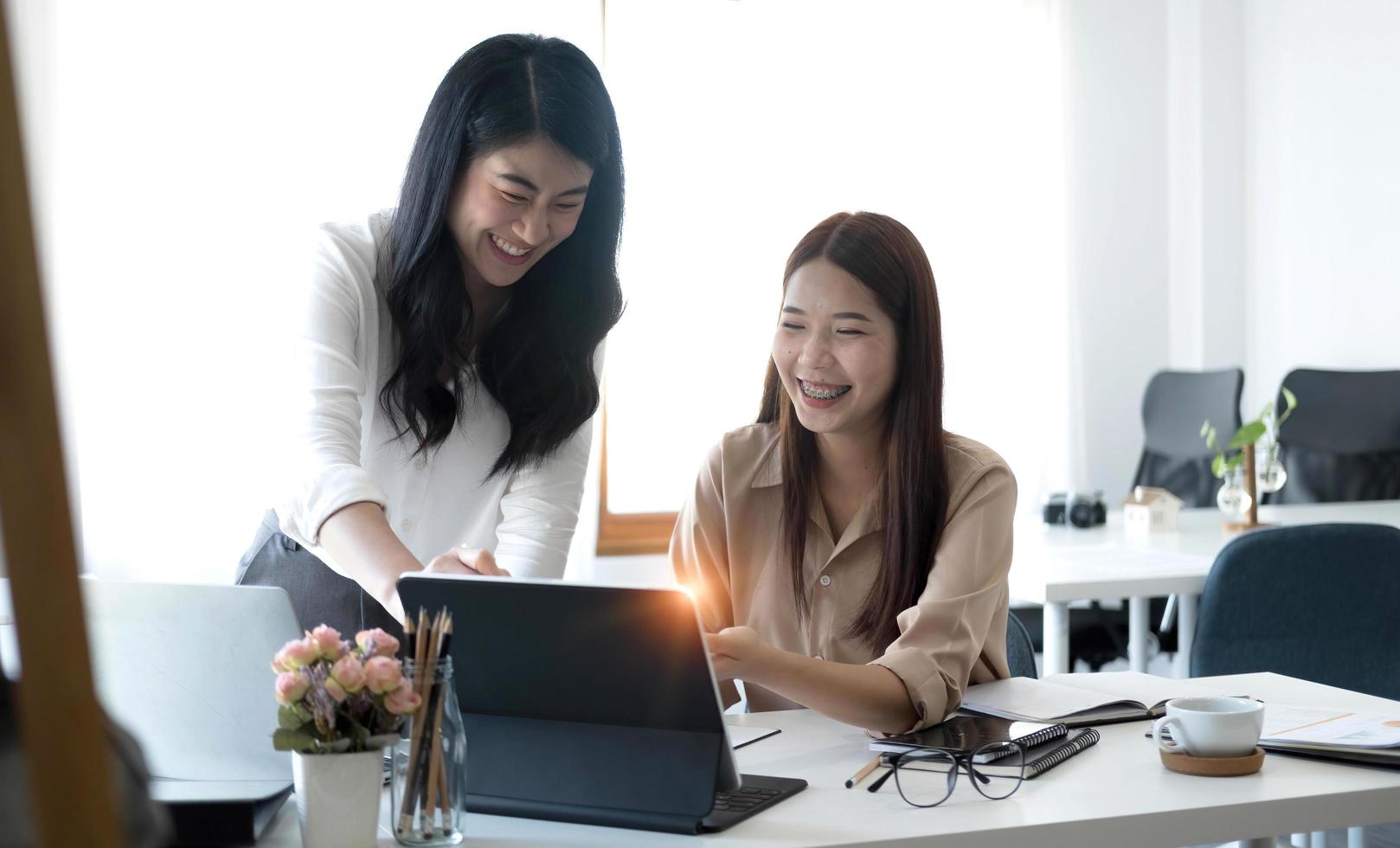 Two young Asian businesswoman discuss investment project working and planning strategy. Business people talking together with laptop computer at office. photo