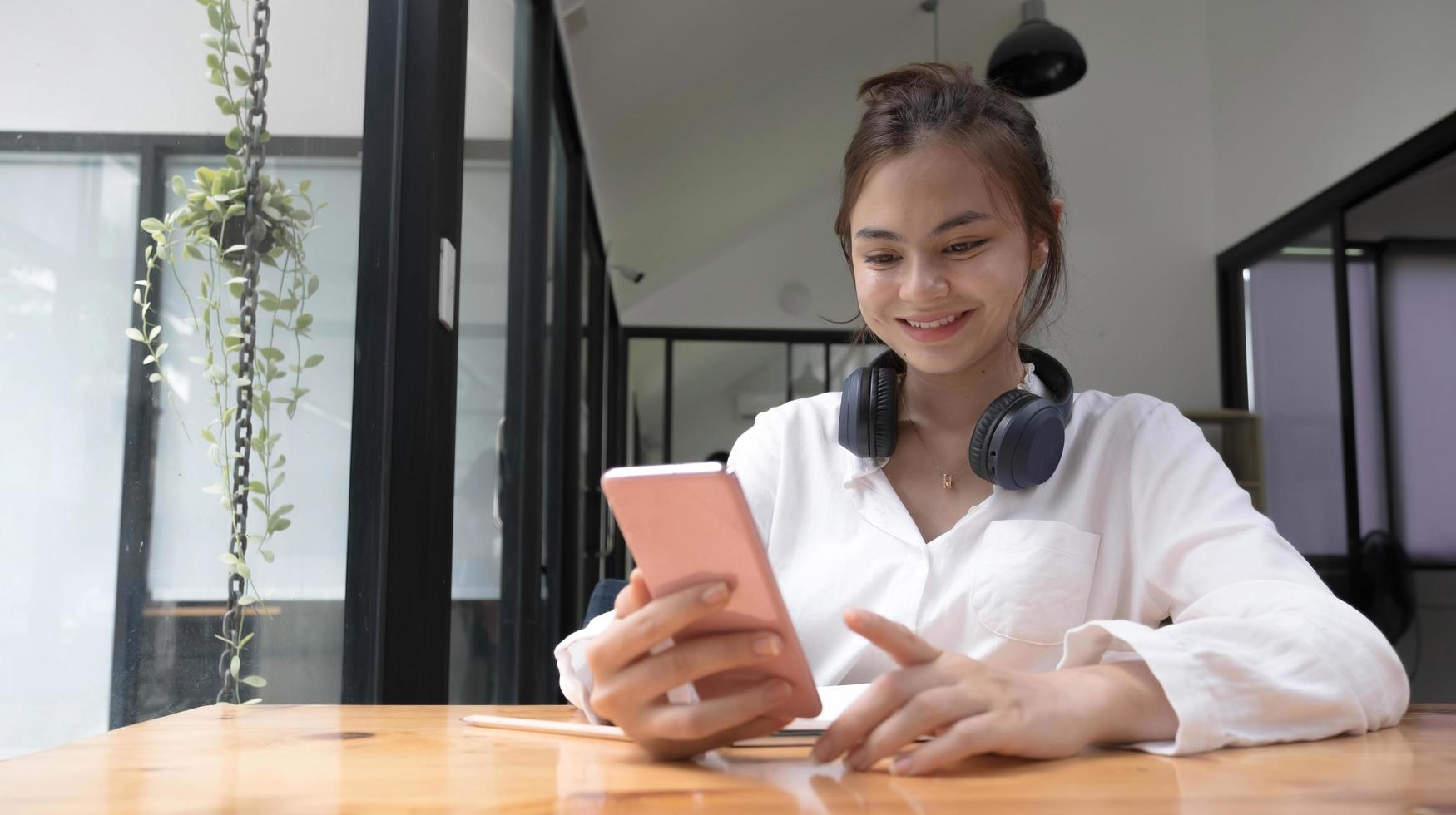 Happy young asian teen girl sit on sofa at home holding phone looking at screen waving hand video calling distance friend online in mobile chat app using smartphone videochat application. photo