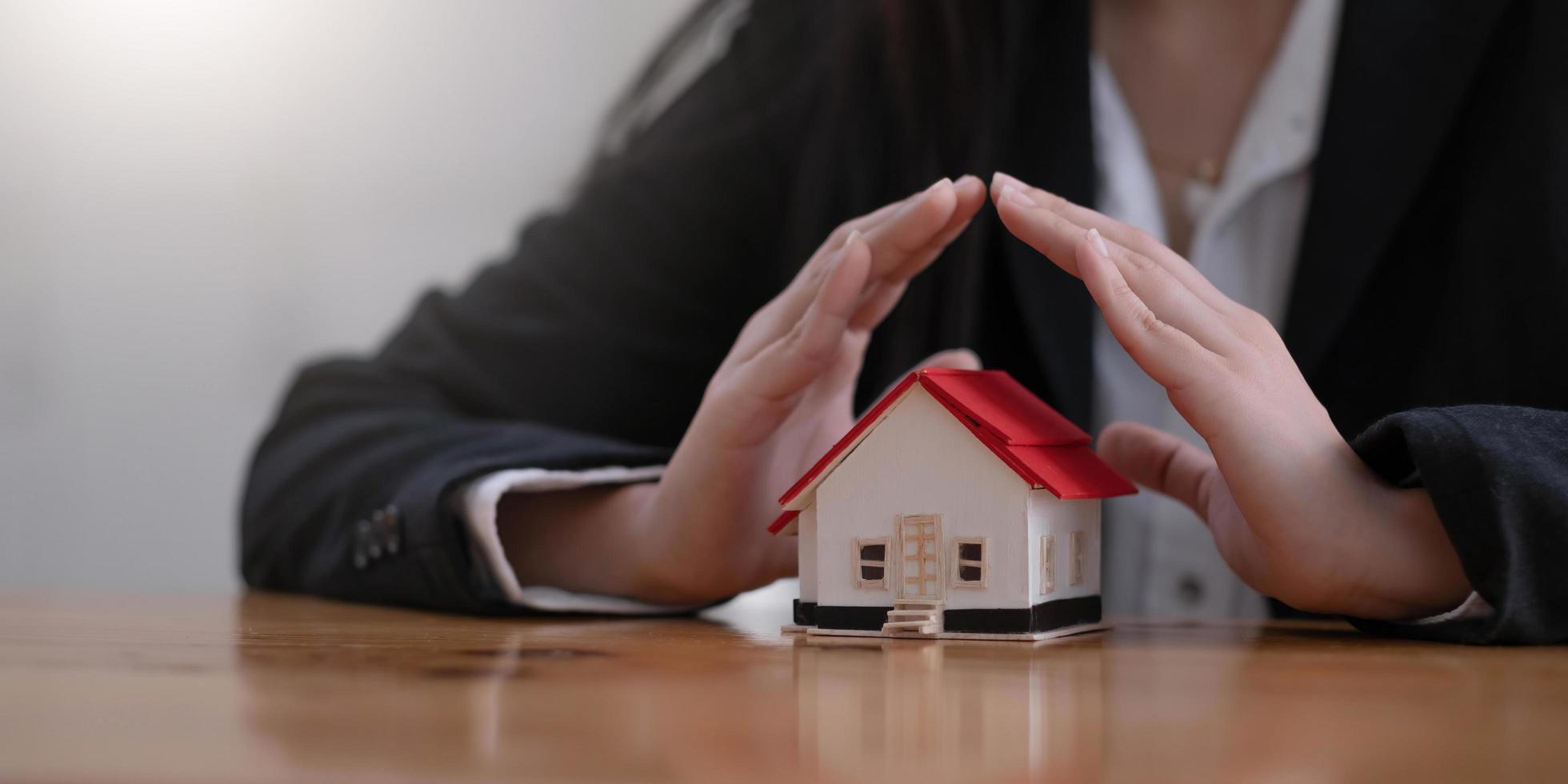 Protect your house concept. Small toy house covered by hands photo