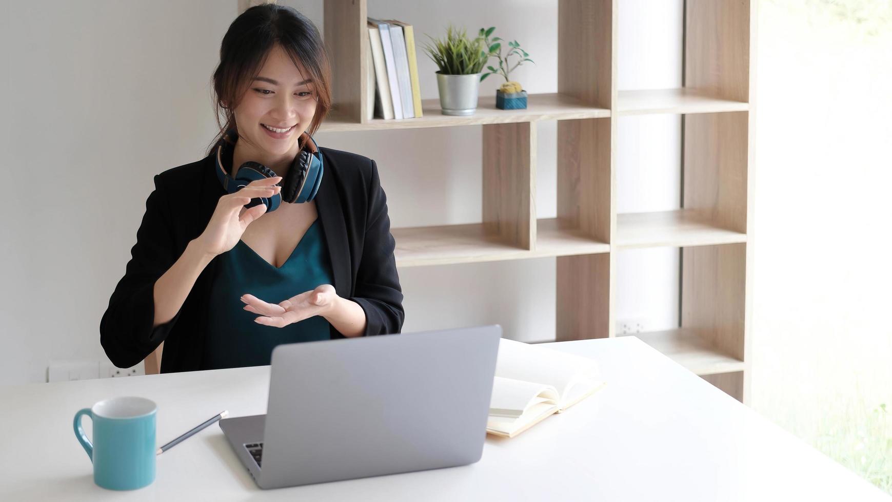 Portrait of a pretty young asian woman studying online with laptop computer while sitting at the table and notebook at home. photo