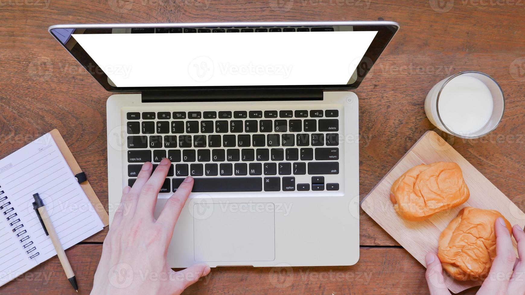 Labtop,notebook,bread and cup of milk with hands on wooden table background. photo
