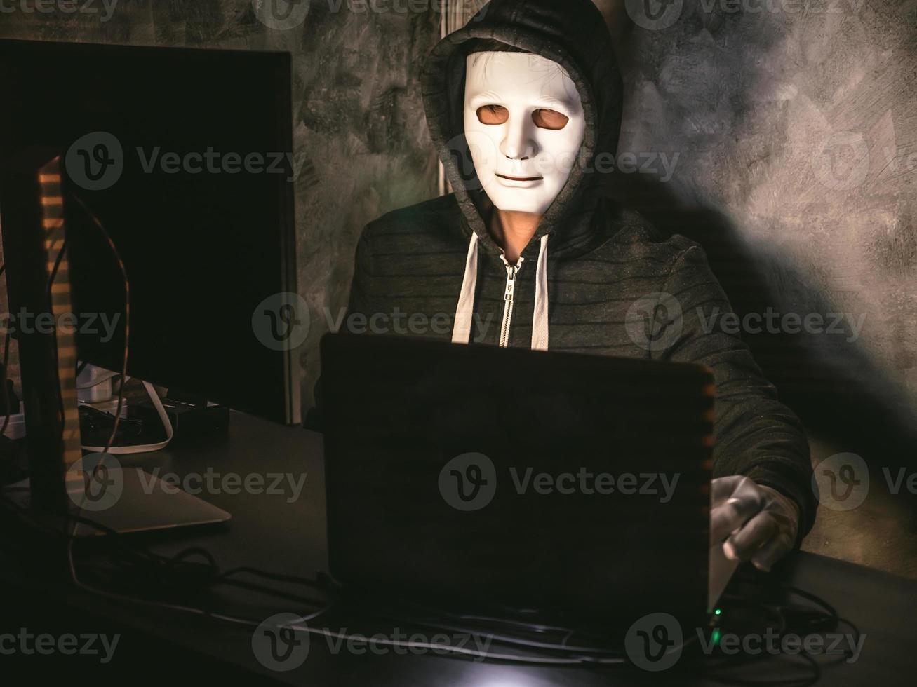 Computer hacker - Man in hoodie shirt with mask stealing data from laptop photo