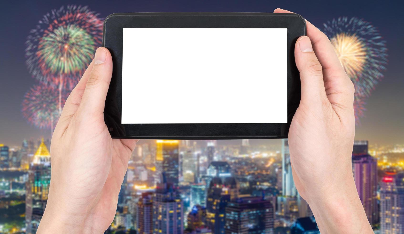 Male hand holding a tablet touch computer gadget with touch blank screen on blurred city landscape and firework background. photo