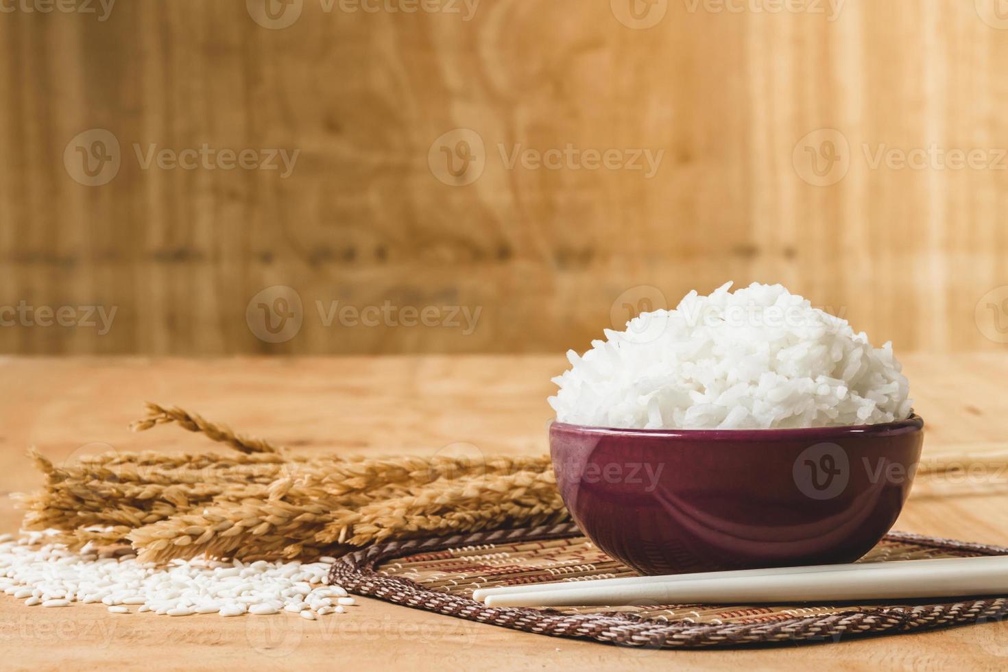 Cooked rice in bowl with raw rice grain and dry rice plant on  wooden table background. photo