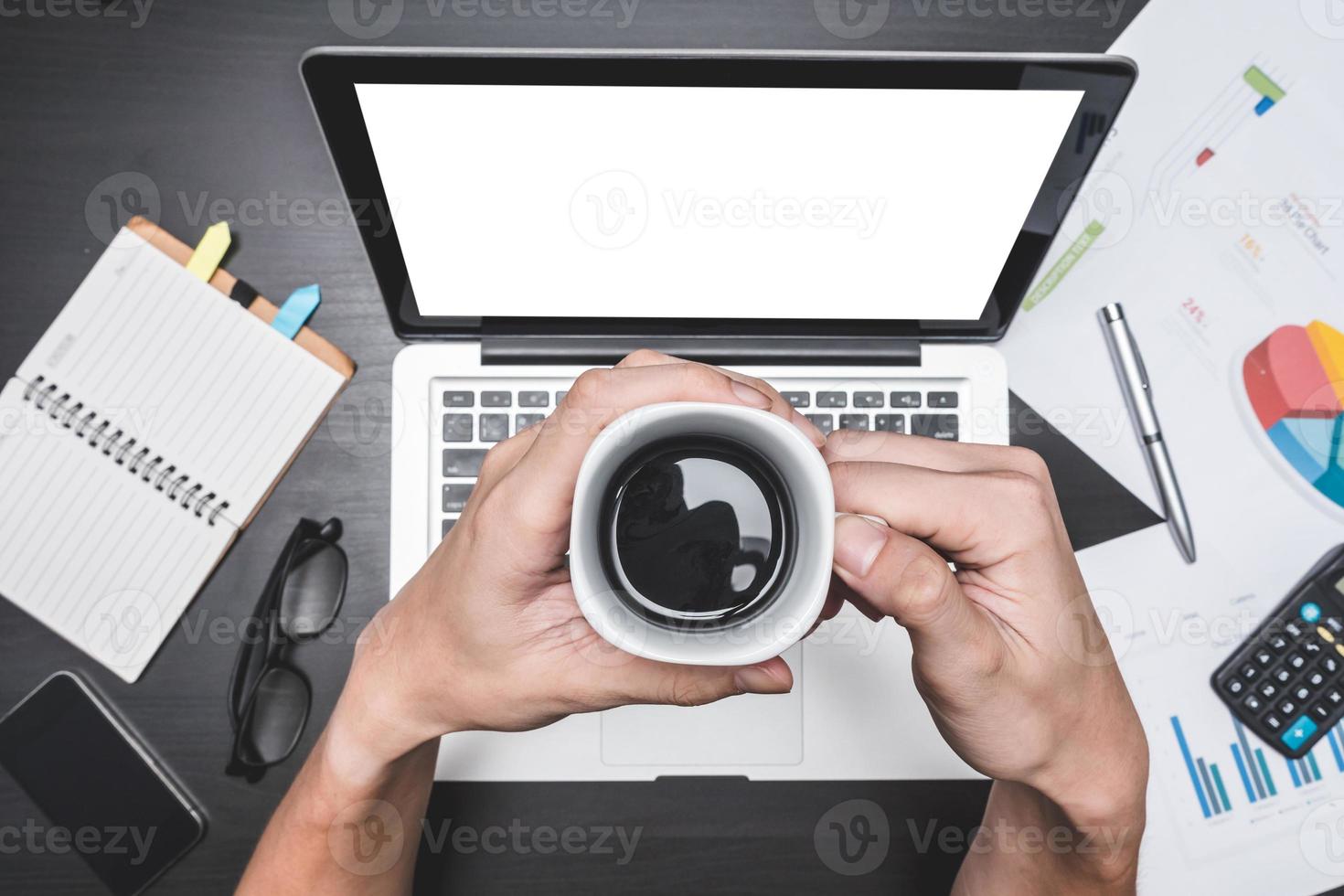 vista superior del lugar de trabajo con laptop y documento, manos masculinas sosteniendo una taza de café, conceptos para análisis de negocios, informe financiero y estrategia. foto