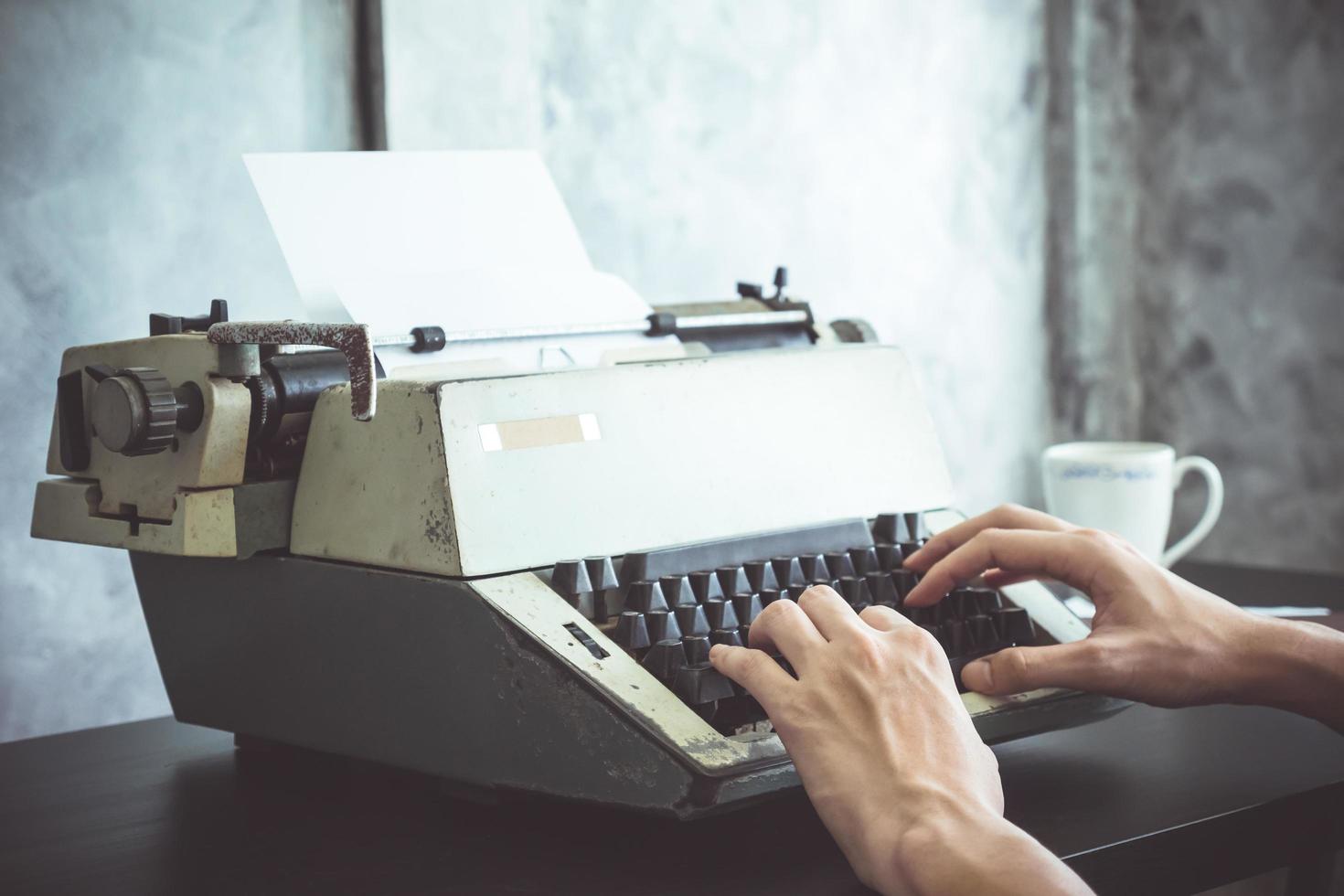 primer plano de manos masculinas escribiendo en máquina de escribir en el escritorio. tono antiguo foto