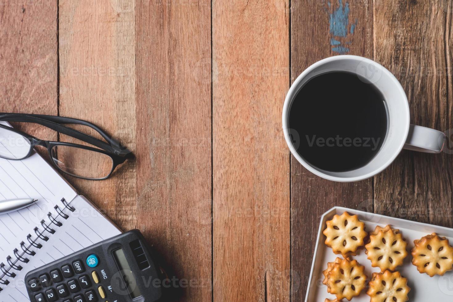 Top view of Notebook with glasses,cookie and coffee cup on wooden table background. Free space for text photo