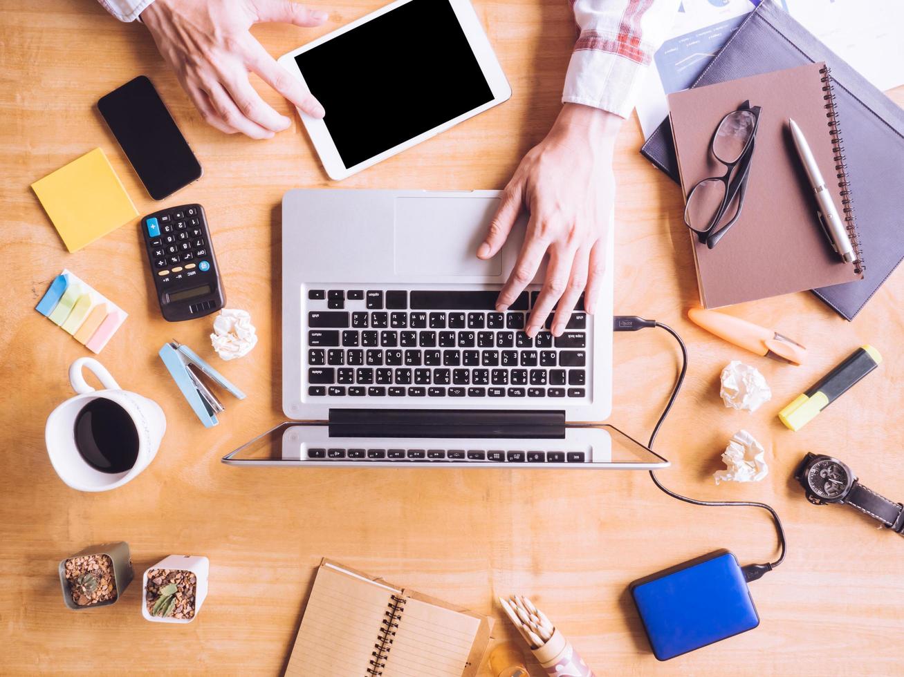 Top view of Male hands using Laptop with Tablet, office supplies on wooden desk. photo