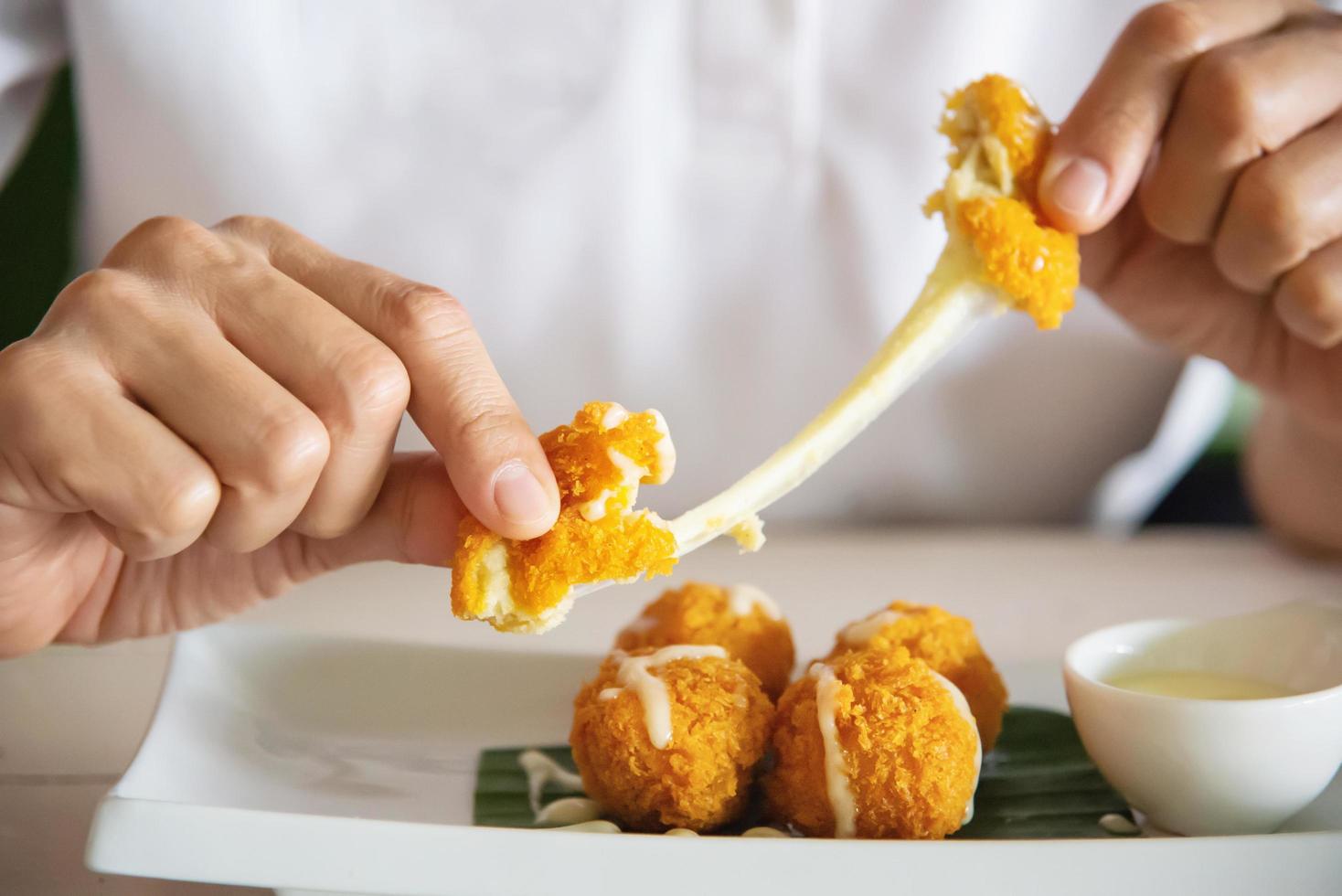 Man is going to eat sticky stretch fried cheese ball. Photo is focused at cheese ball