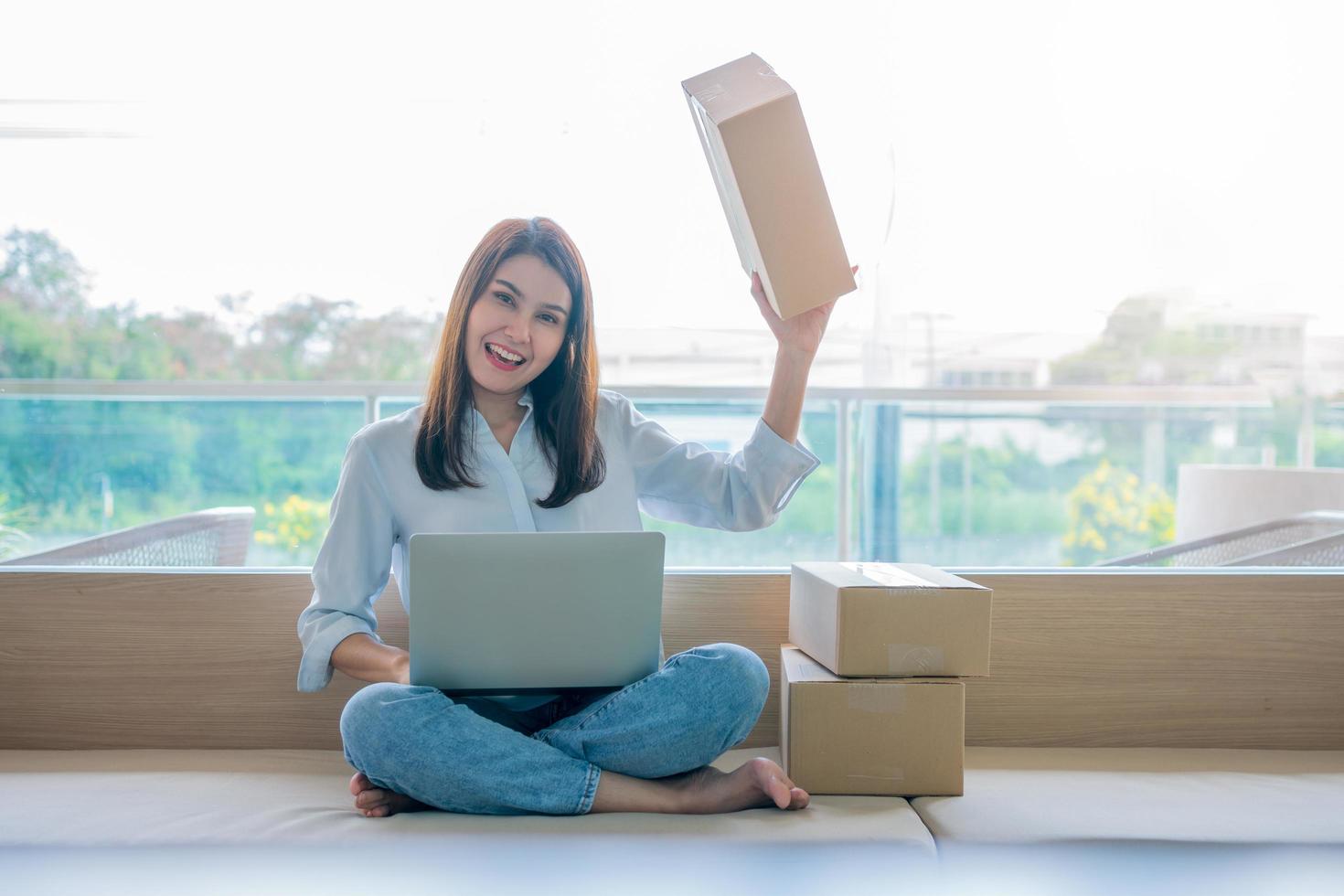 Happy young Asian woman entrepreneur, Smile for sales success after checking order from online shopping store in a laptop at home office, Concept of merchant business online and eCommerce photo
