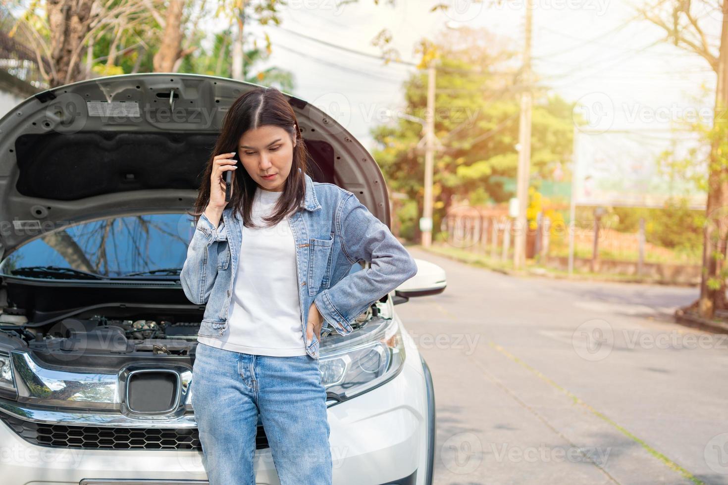 mujer asiática enojada y usando un teléfono móvil pidiendo ayuda después de una avería en el coche en la calle. concepto de problema del motor del vehículo o accidente y ayuda de emergencia de un mecánico profesional foto