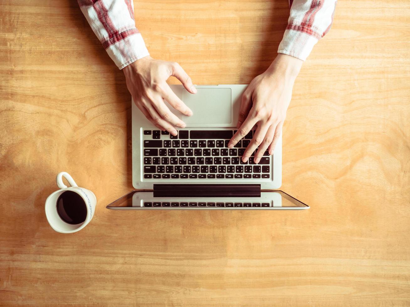 Top view of Male using Laptop with a cup of coffee on wooden table background. photo