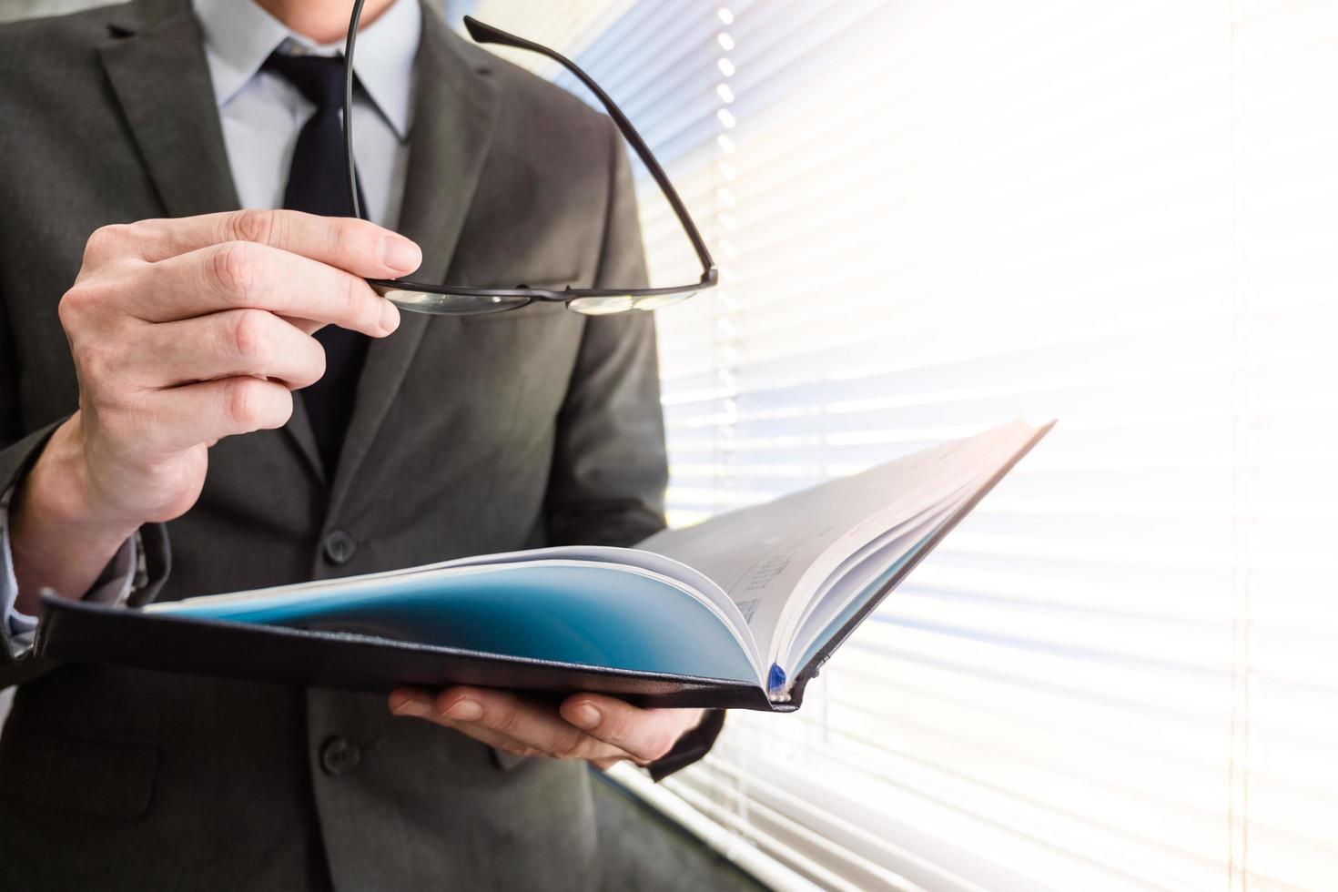 Close up of businessman reading notebook while standing at a window in an office photo