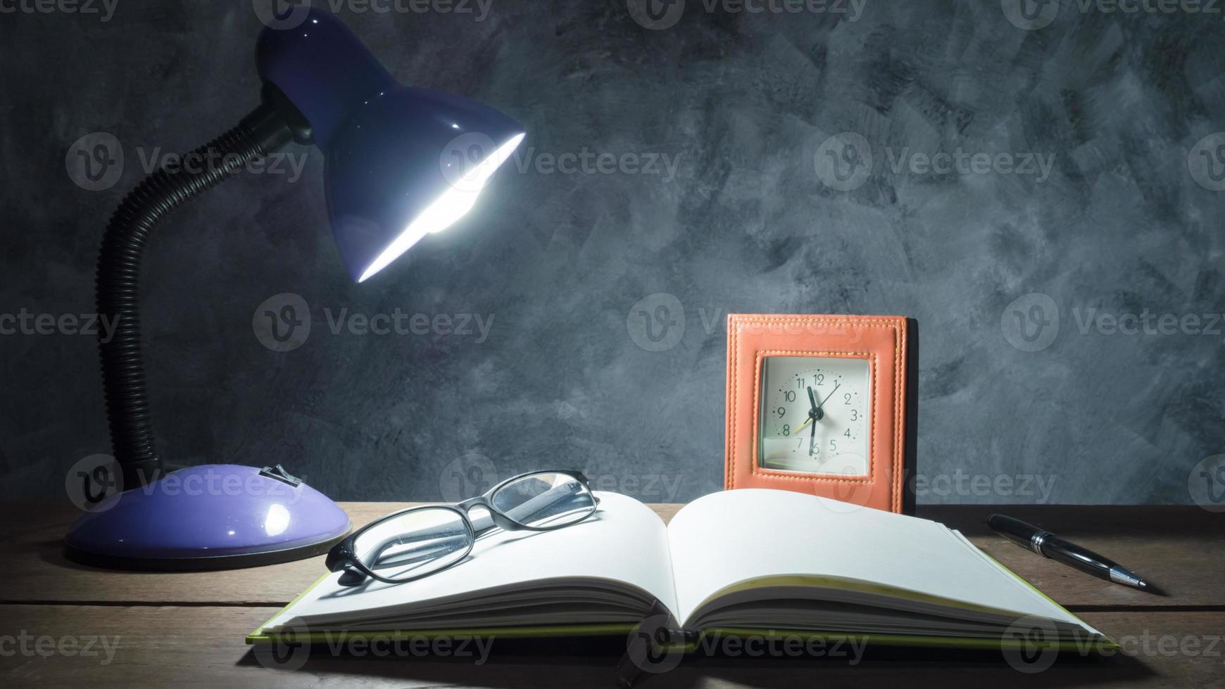 Lamp with notebook,pen,clock and glasses  on  wooden table with vintage wall background. photo