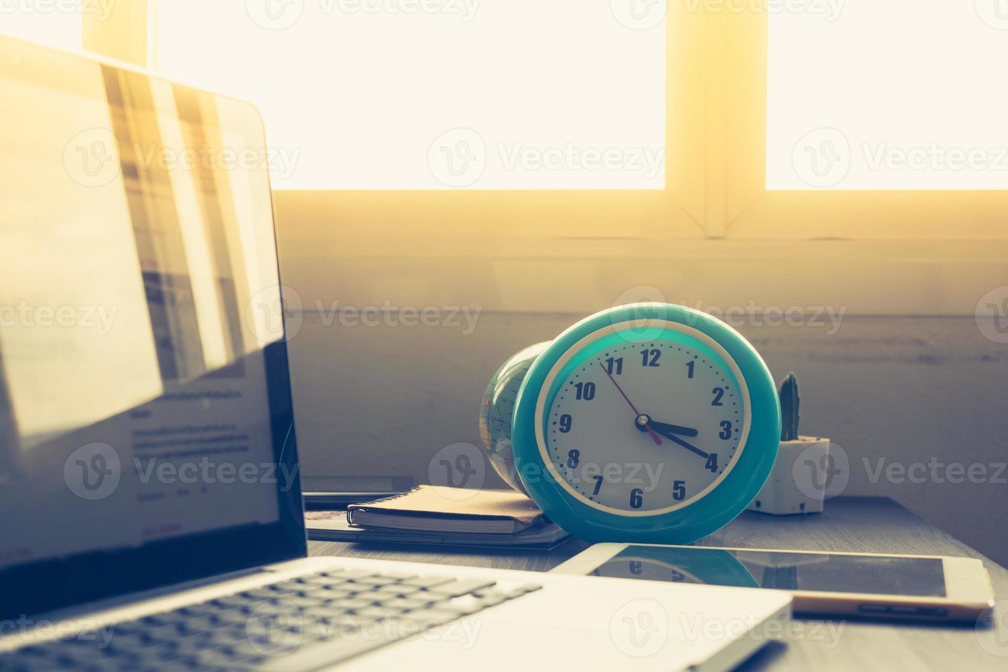 Clock with Laptop on office desk and sunshine in afternoon. photo