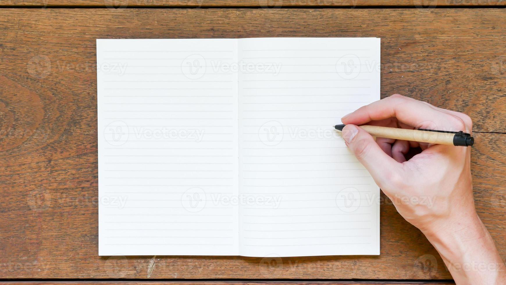 Man hands with pen writing on empty notepad over wooden table. photo