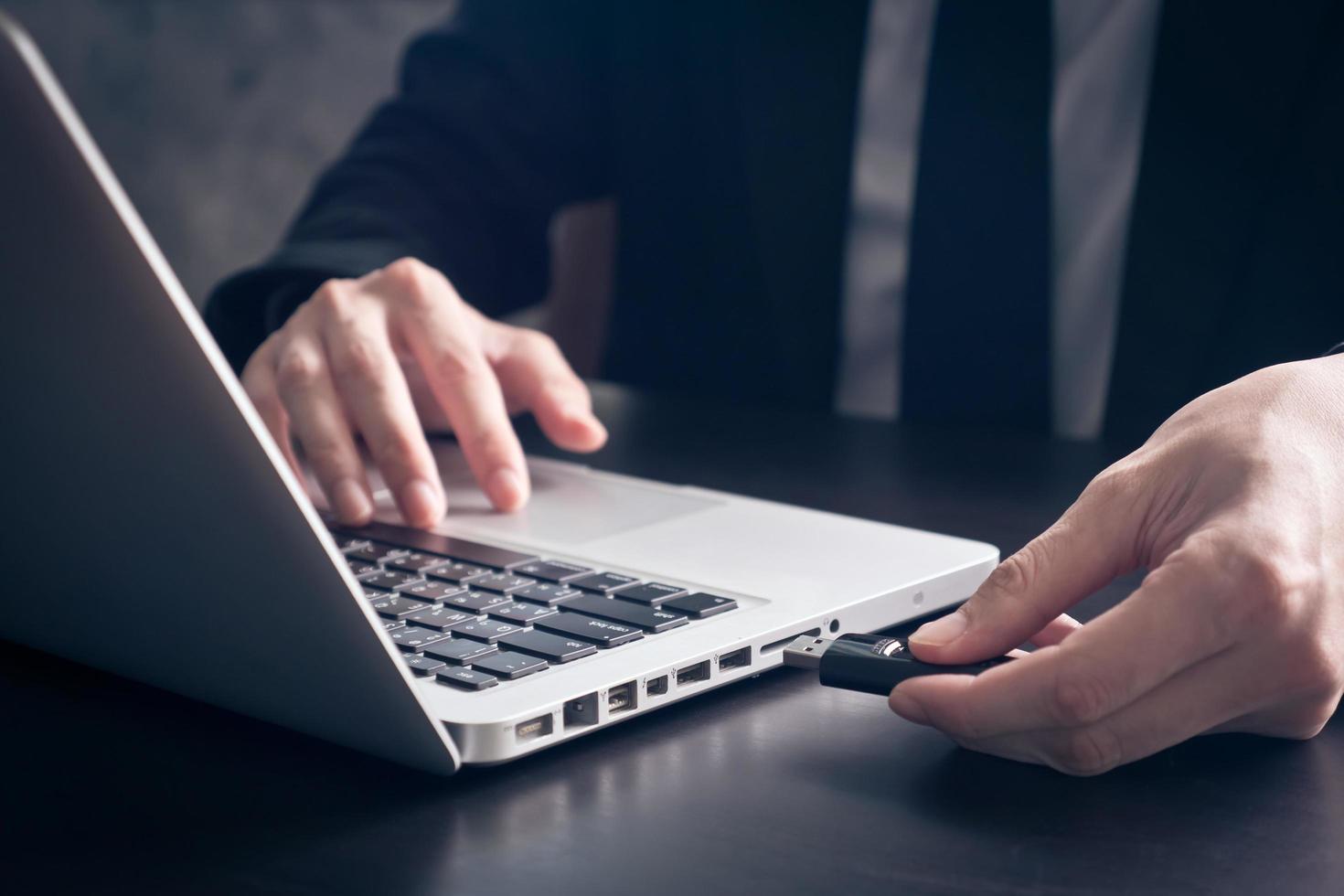 primer plano de un hombre de negocios que usa una unidad flash para conectarse a una computadora portátil en el escritorio de la oficina. foto